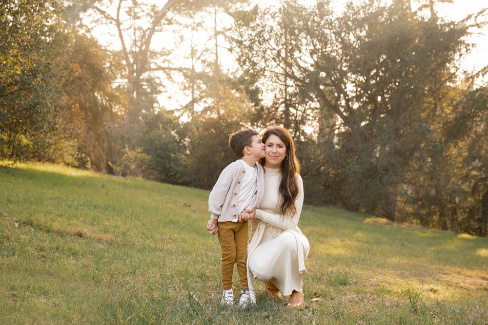 Young boy giving his mother a sweet kiss on the cheek in a sunlit grassy park.