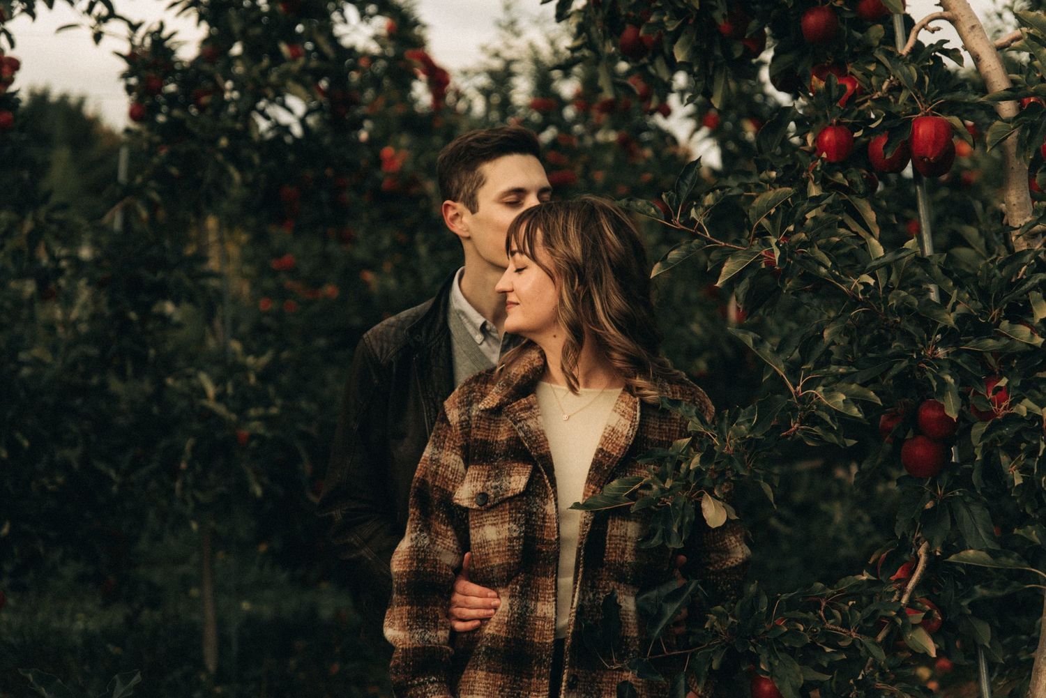 Intimate moment captured between couple in plaid flannel among apple trees.