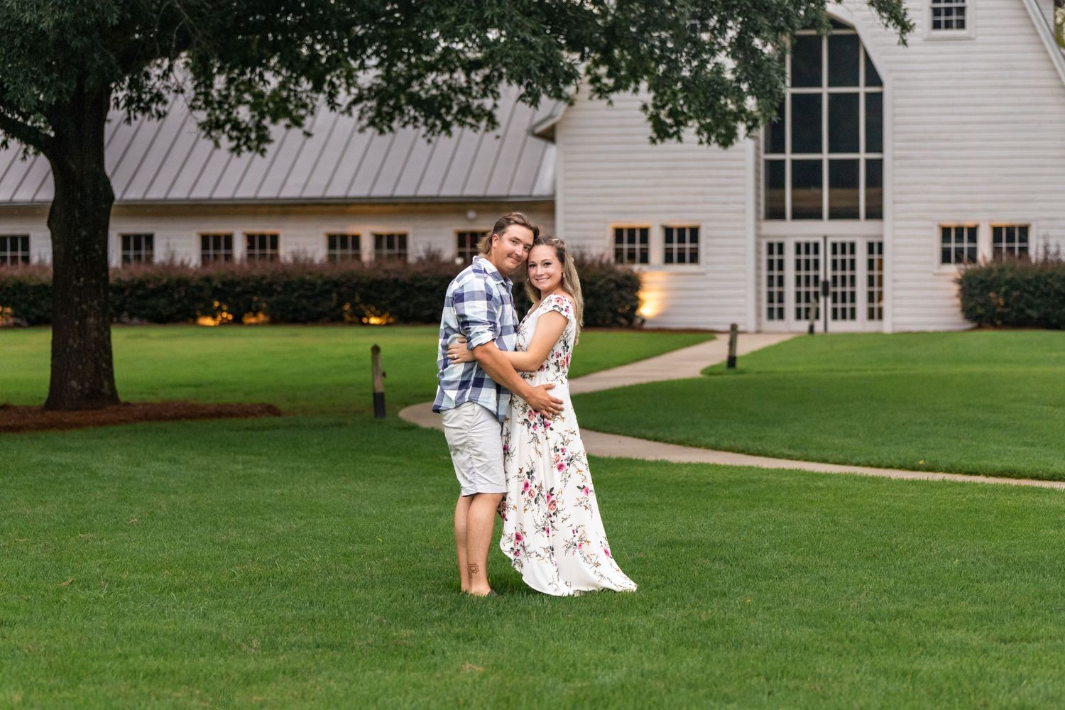 Couple embracing on manicured lawn with white church building in background.