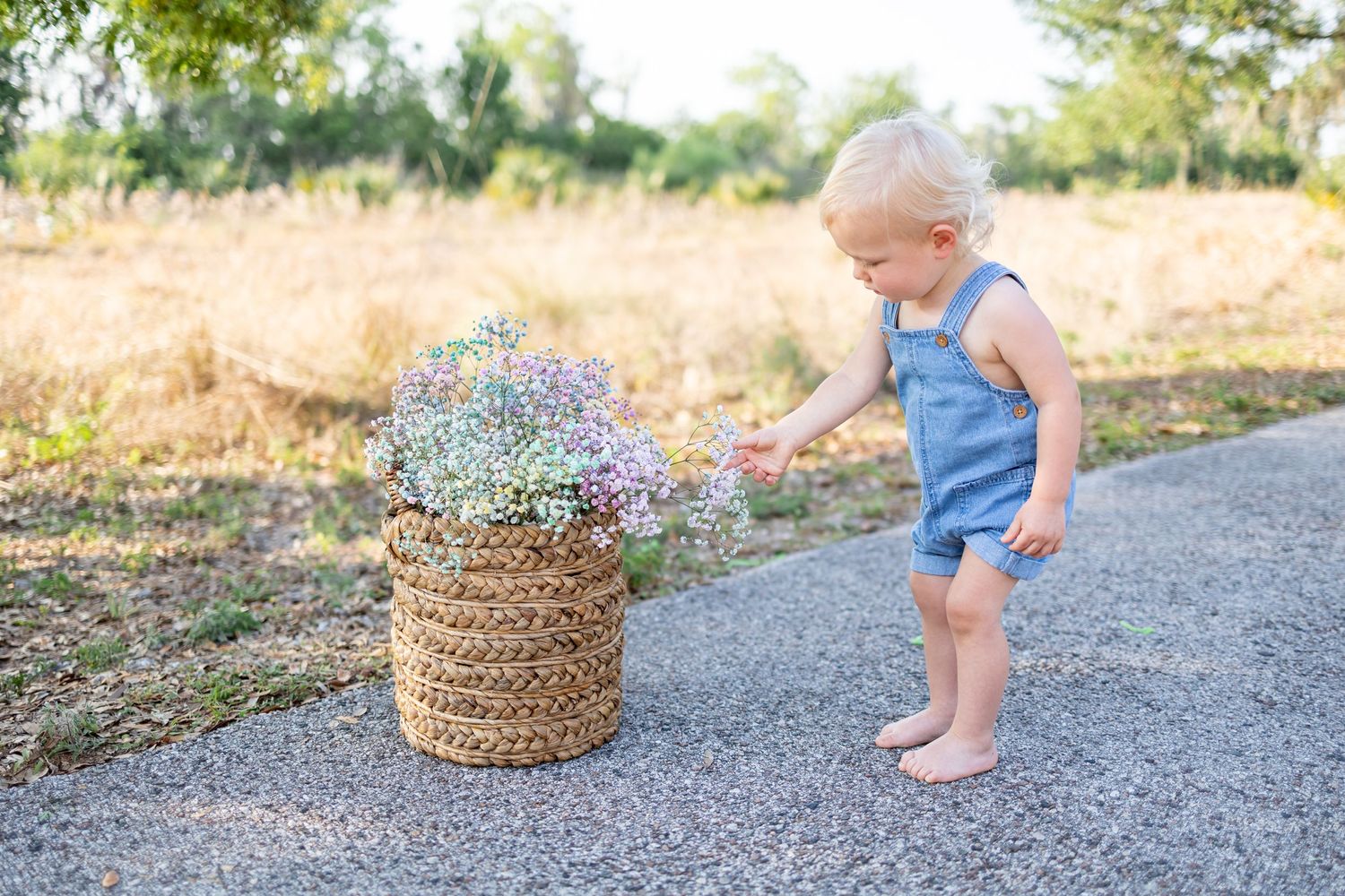Baby plays near woven basket on gravel path during outdoor photo session.