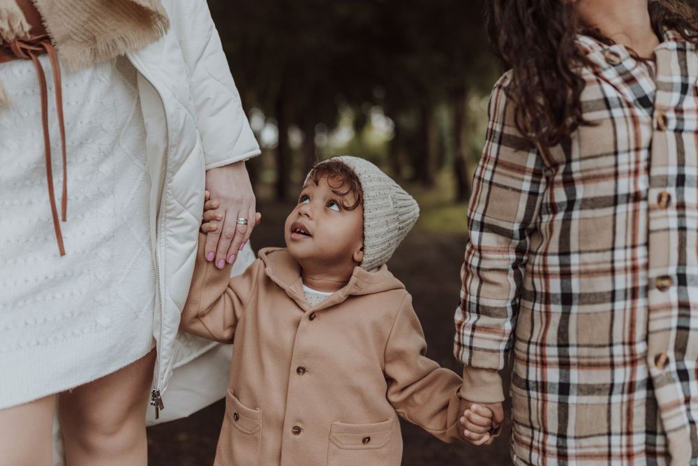 A small child in a beanie looks up adoringly while holding hands with family members.