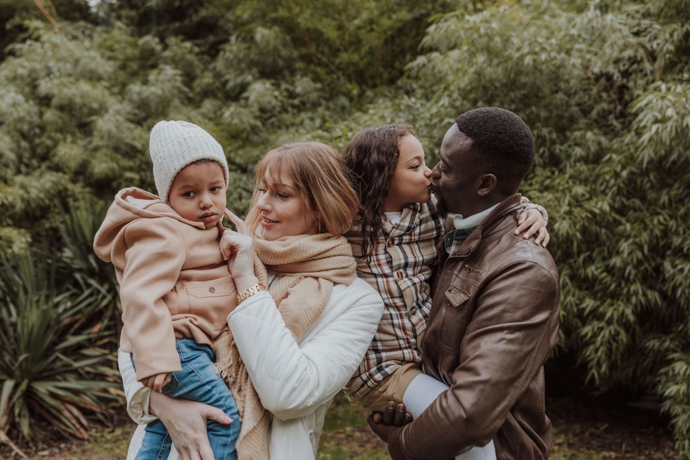 Family embracing outdoors against a backdrop of green foliage on a winter day.