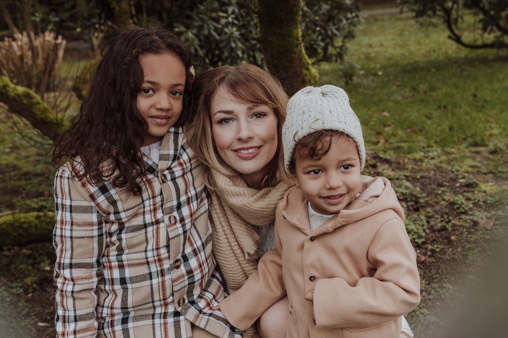 Three people smile together in a close family portrait outdoors.