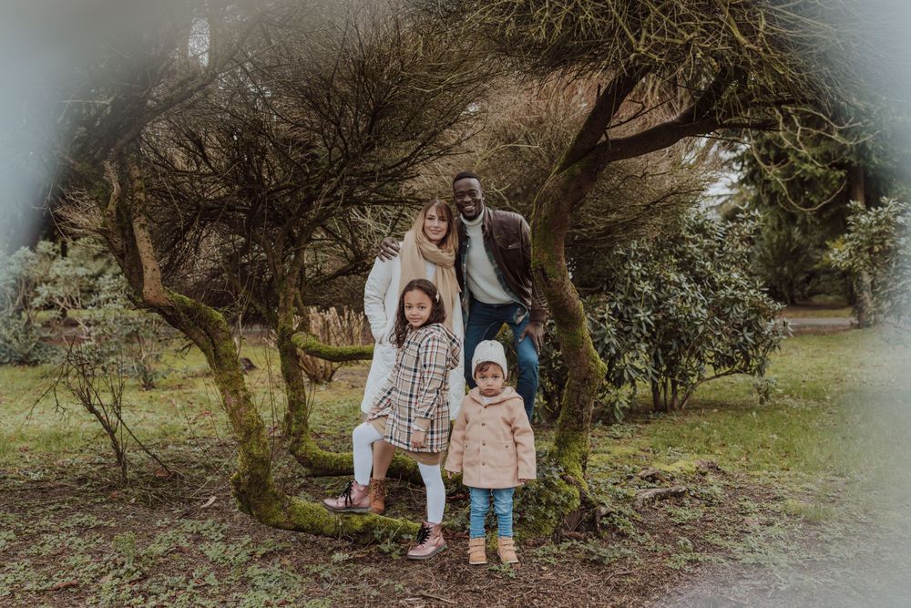 A family poses together under a tree branch in a park setting with moody lighting.