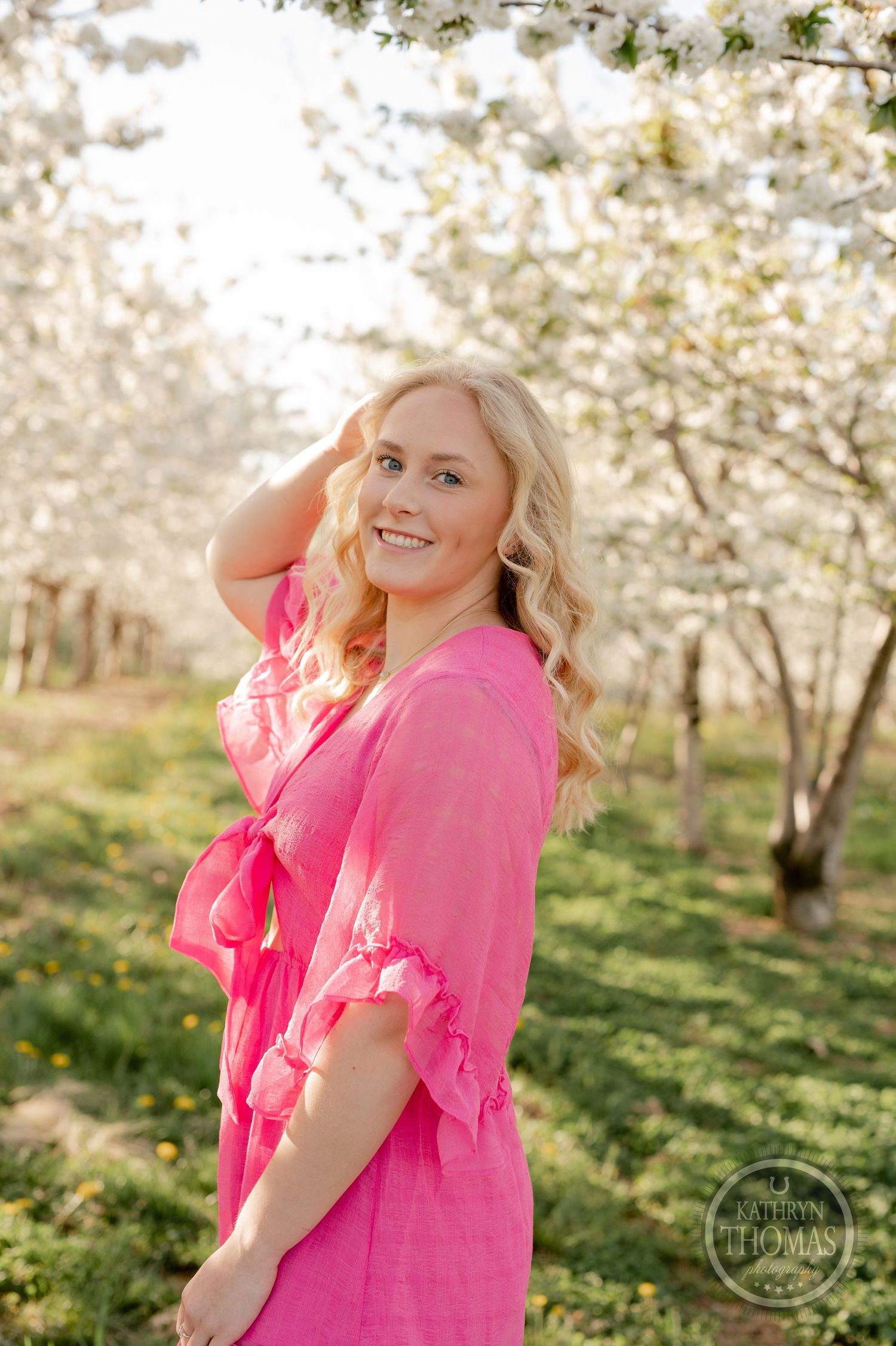 A spring photoshoot in a blooming cherry orchard featuring a pink wrap dress against white blossoms.