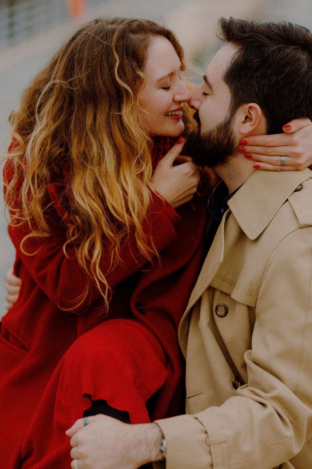 Intimate portrait of couple embracing, with red and beige coats creating striking contrast.