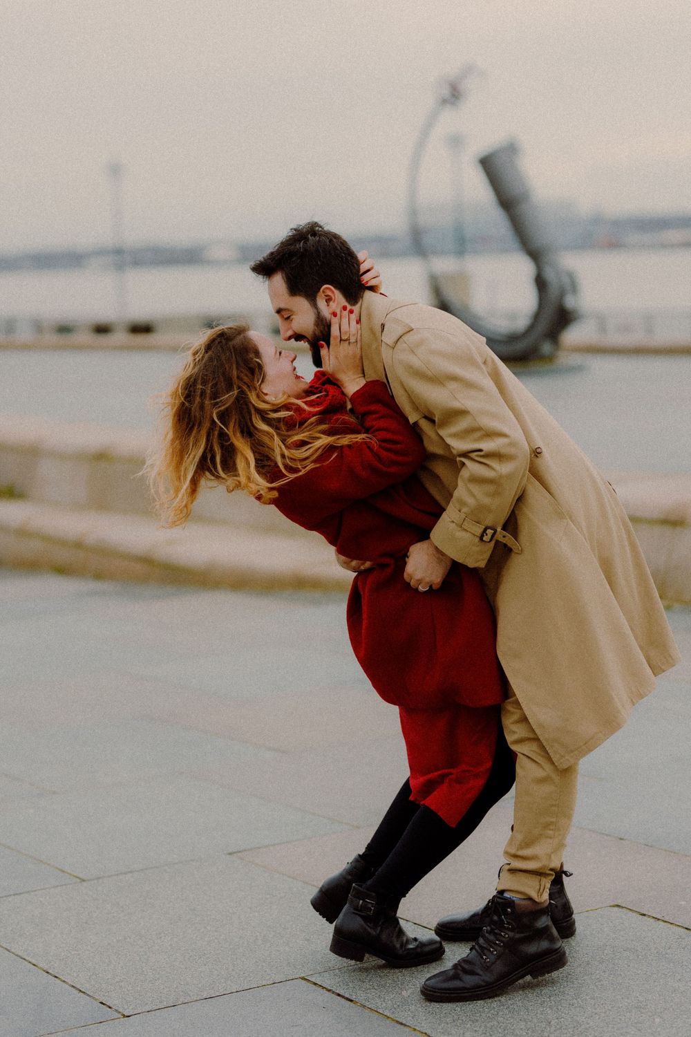 Dancing couple in coordinated red and beige coats dip dramatically on urban walkway.