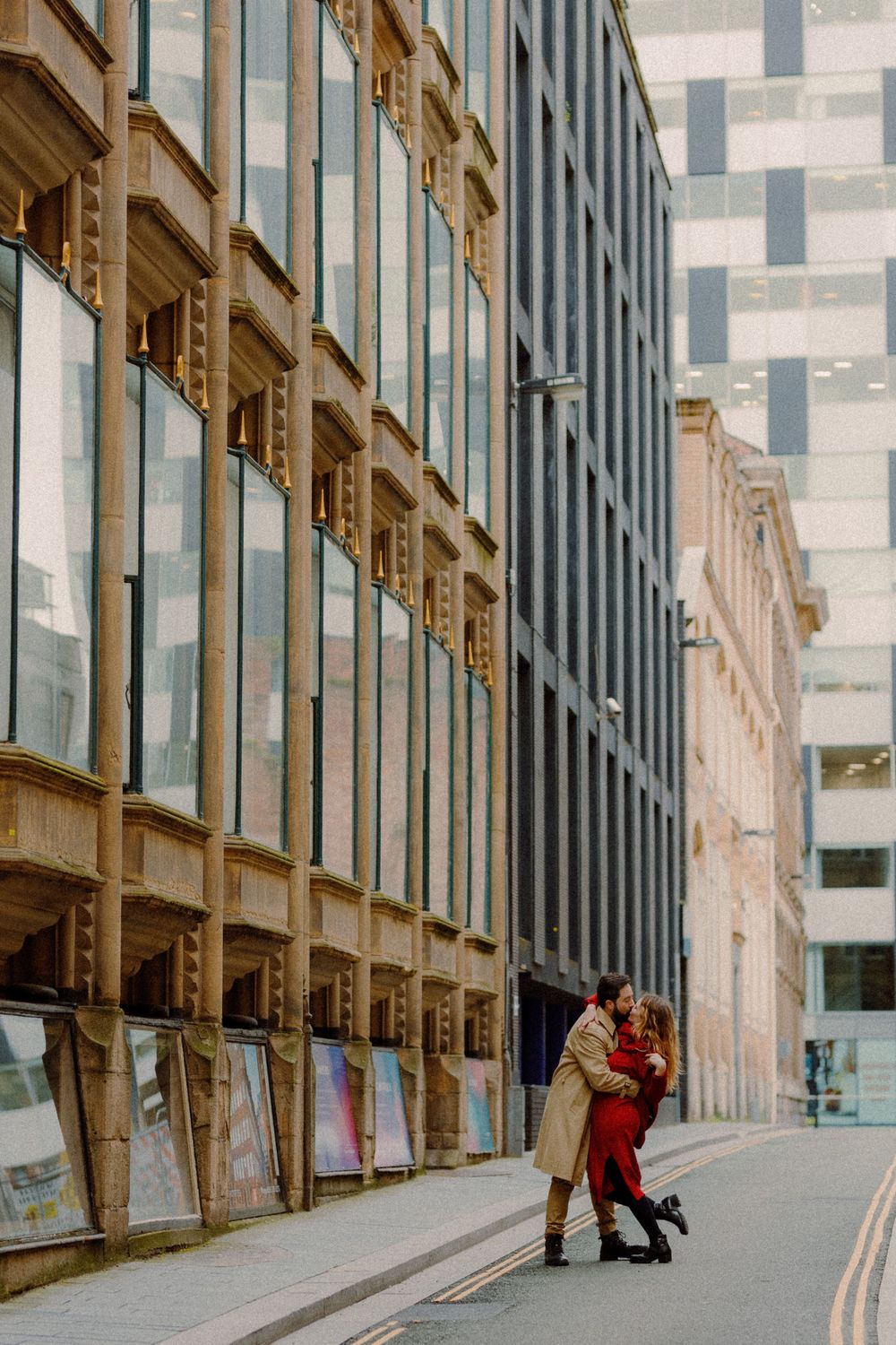 A couple in contrasting coats share an intimate moment against modern architecture.