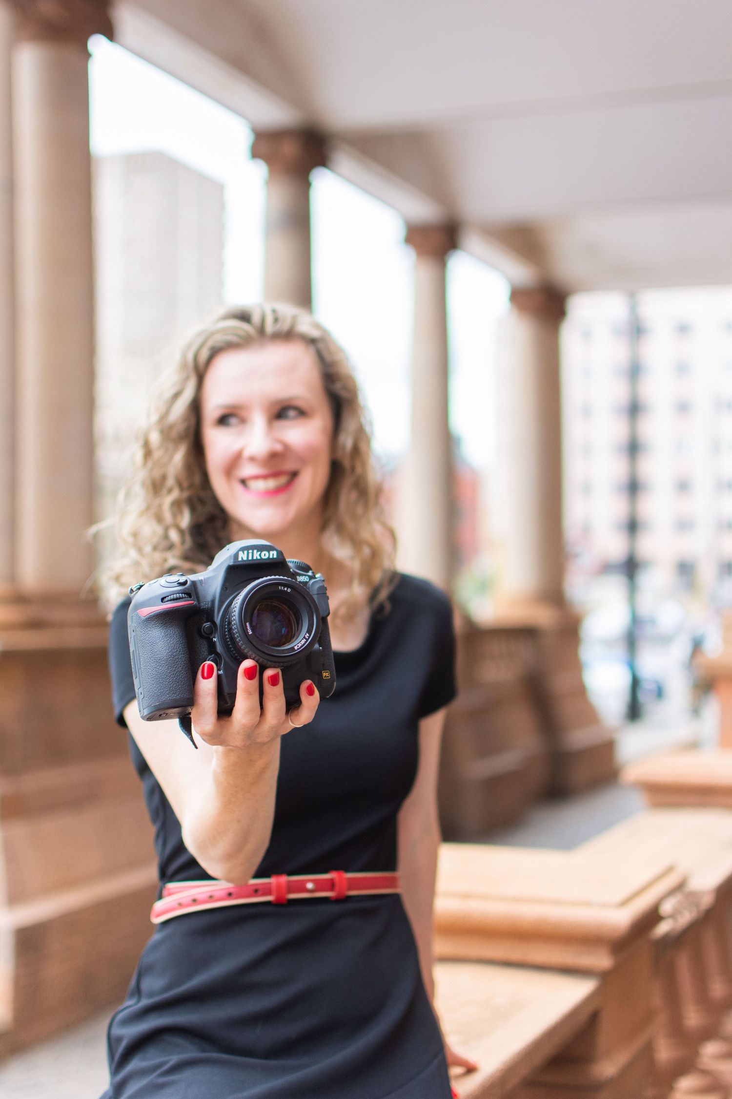 Photographer holding professional DSLR camera in elegant colonnade setting.