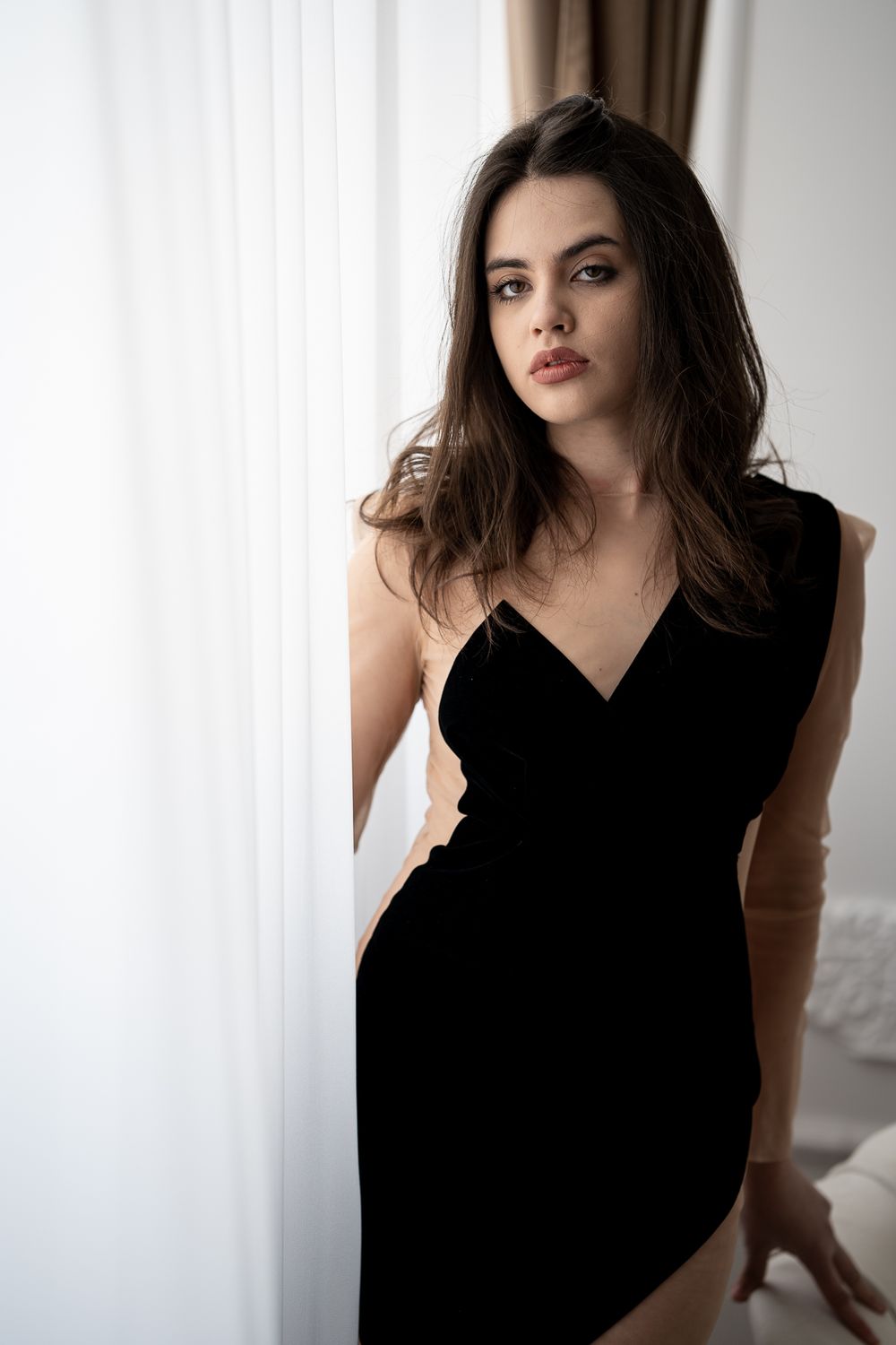 Model in black sleeveless dress poses dramatically in studio lighting.