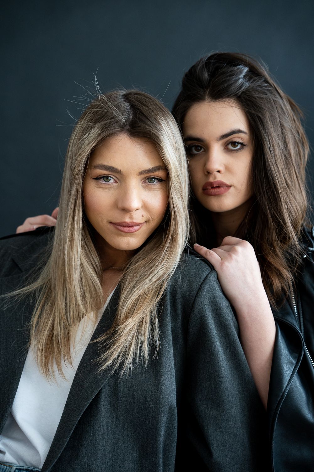 Two models in contrasting styles pose together against dark background.