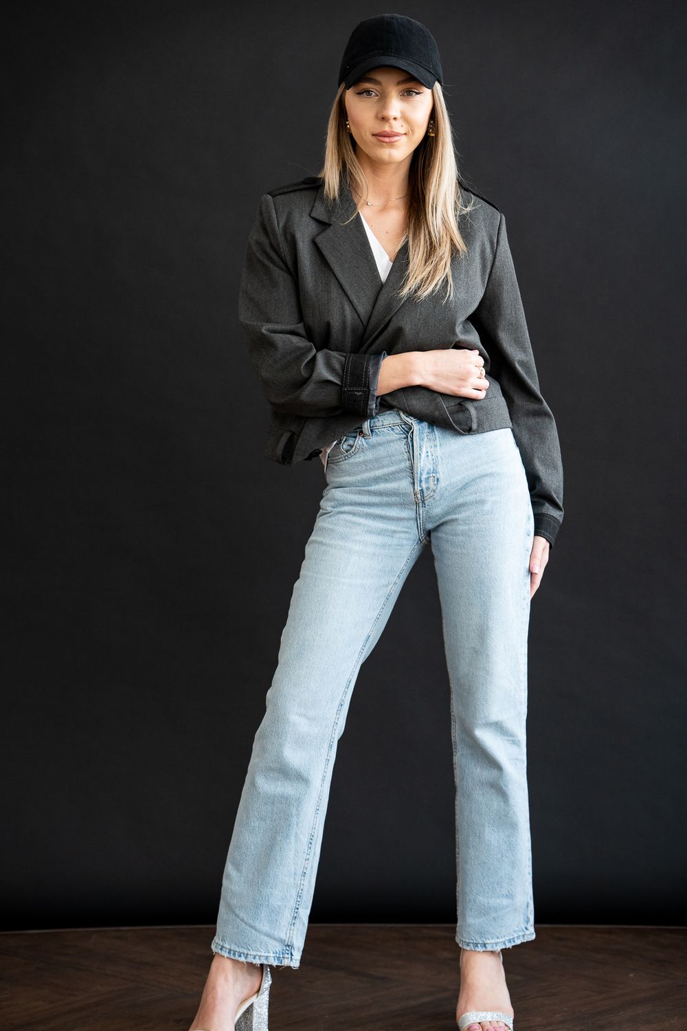 Model wearing casual denim and blazer poses against dark backdrop.
