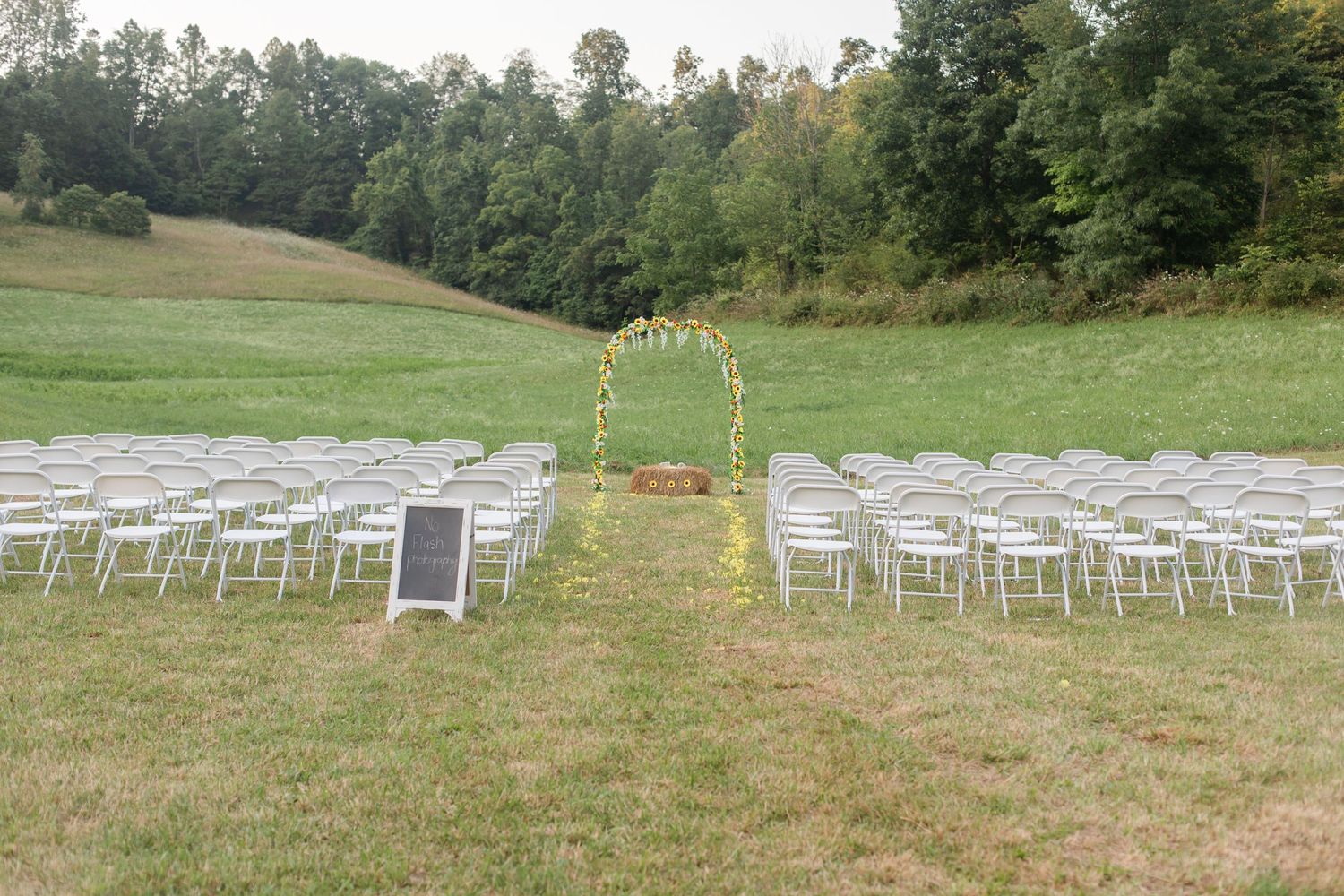 Outdoor wedding ceremony setup with white chairs arranged in rows on a grassy hillside.