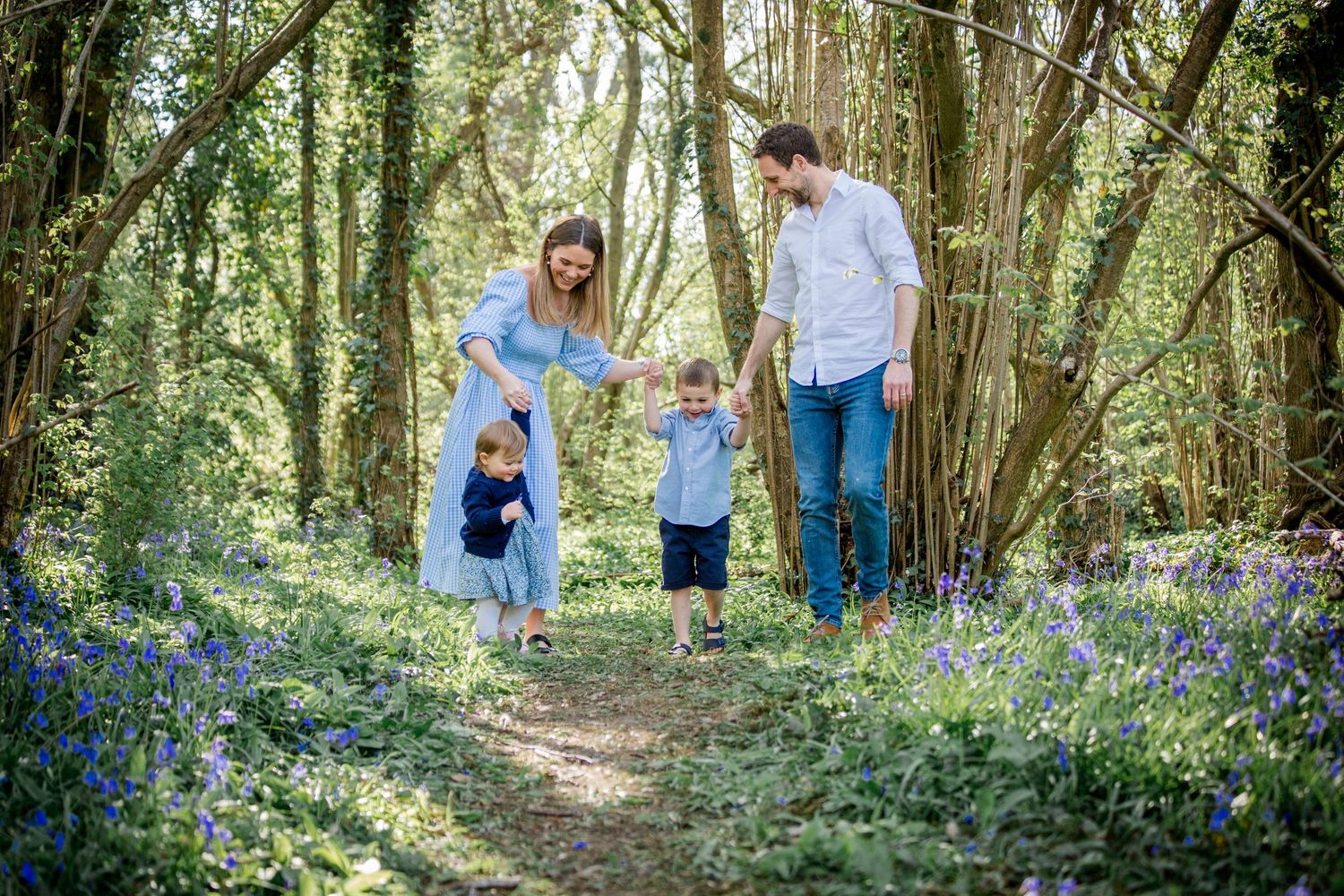 mother, preschooler, toddler and father walking through the bluebells