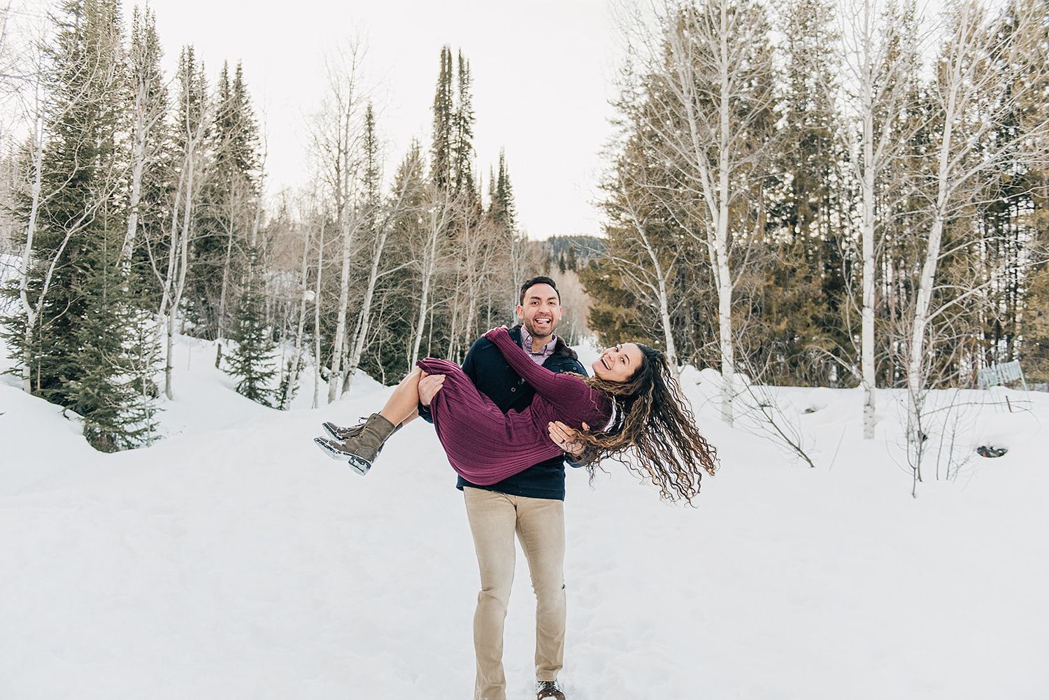 A playful winter moment captured as a couple spins in the snow surrounded by aspen trees.