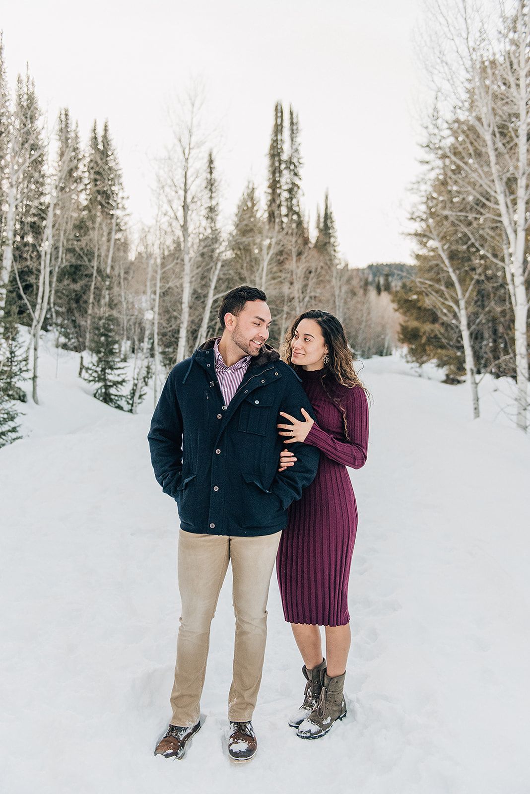 A romantic winter portrait of a couple standing in snow surrounded by aspen and pine trees.