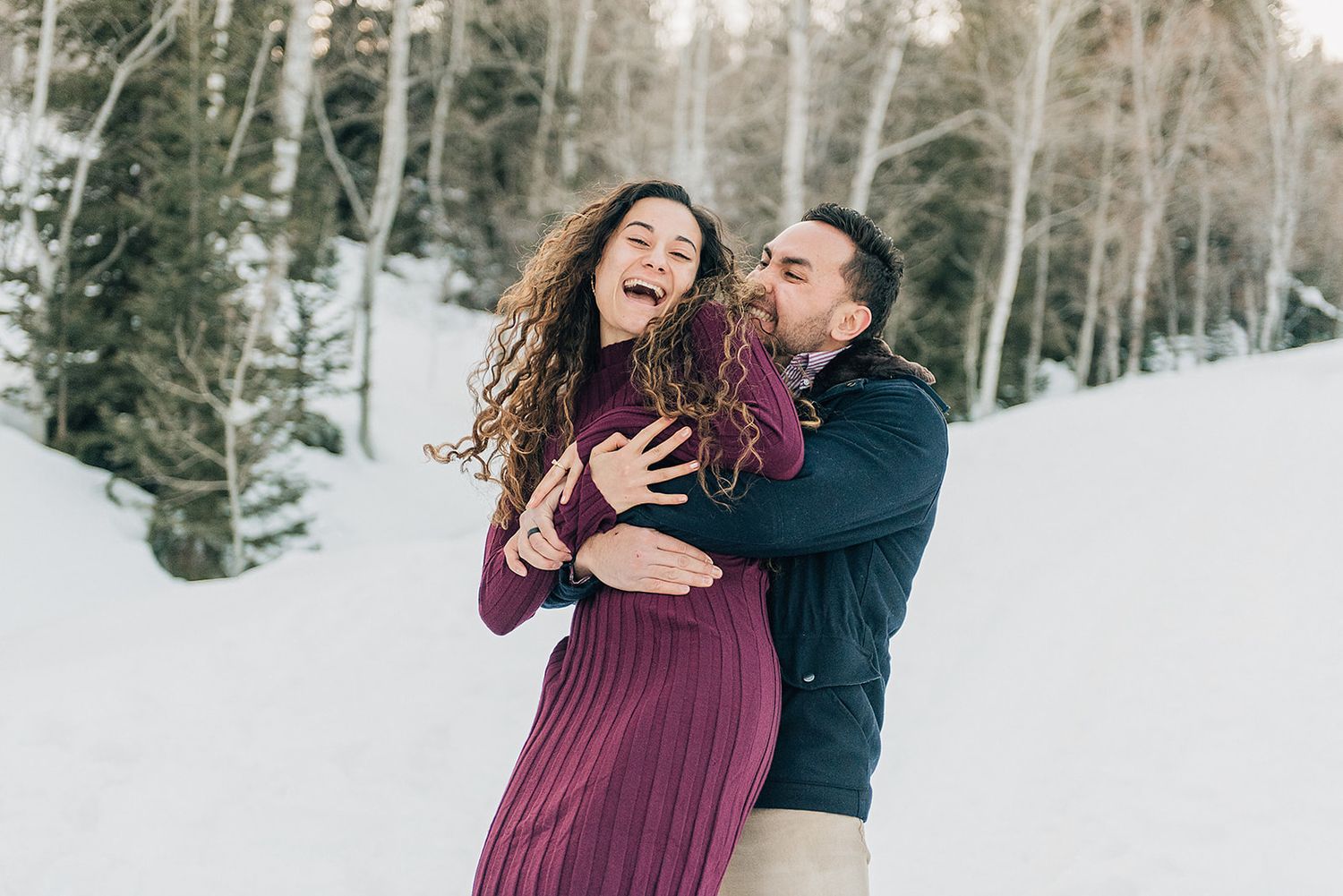 Joyful embrace between couple in winter scene with aspen trees.
