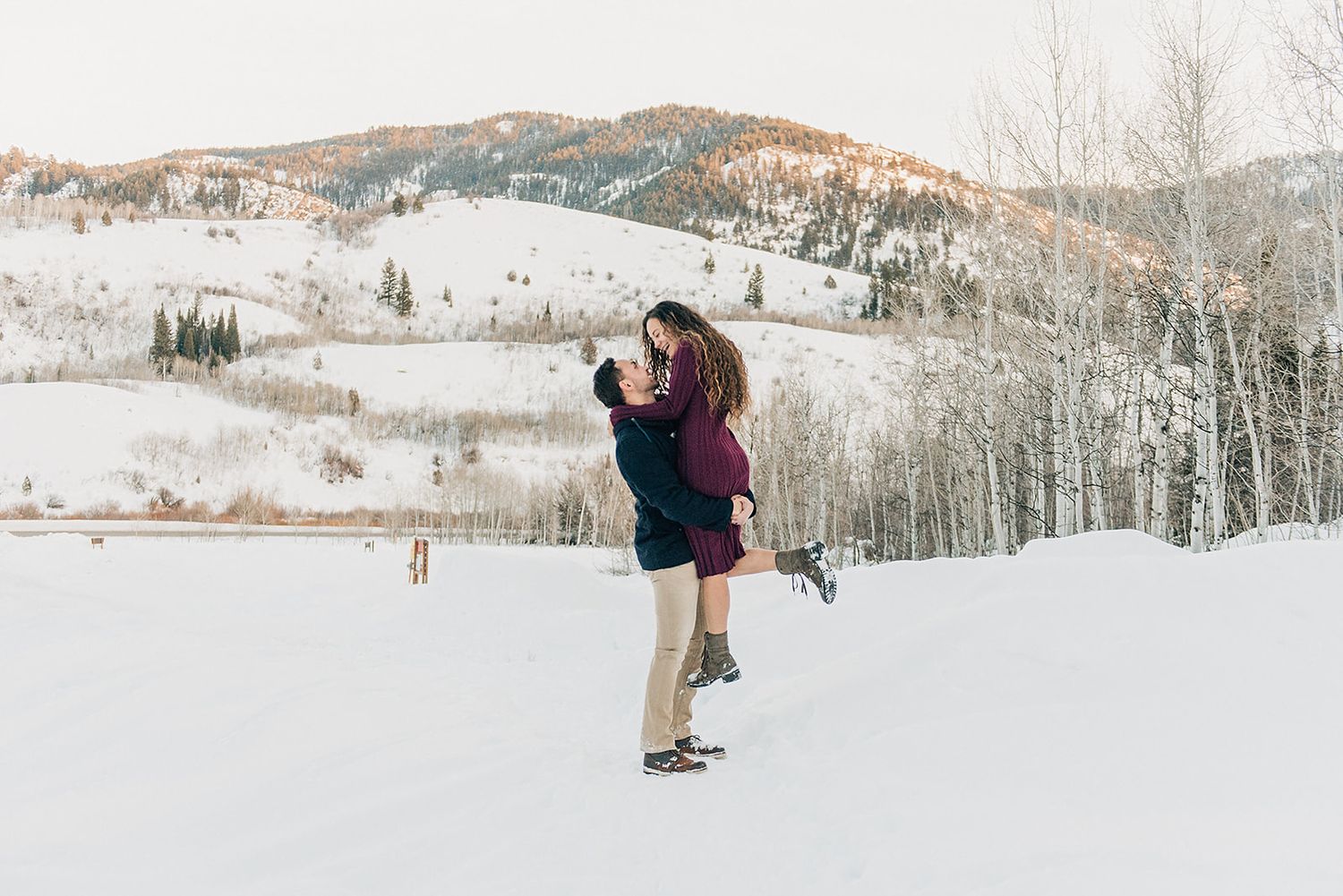 Romantic lift pose in snowy mountain landscape at sunset.