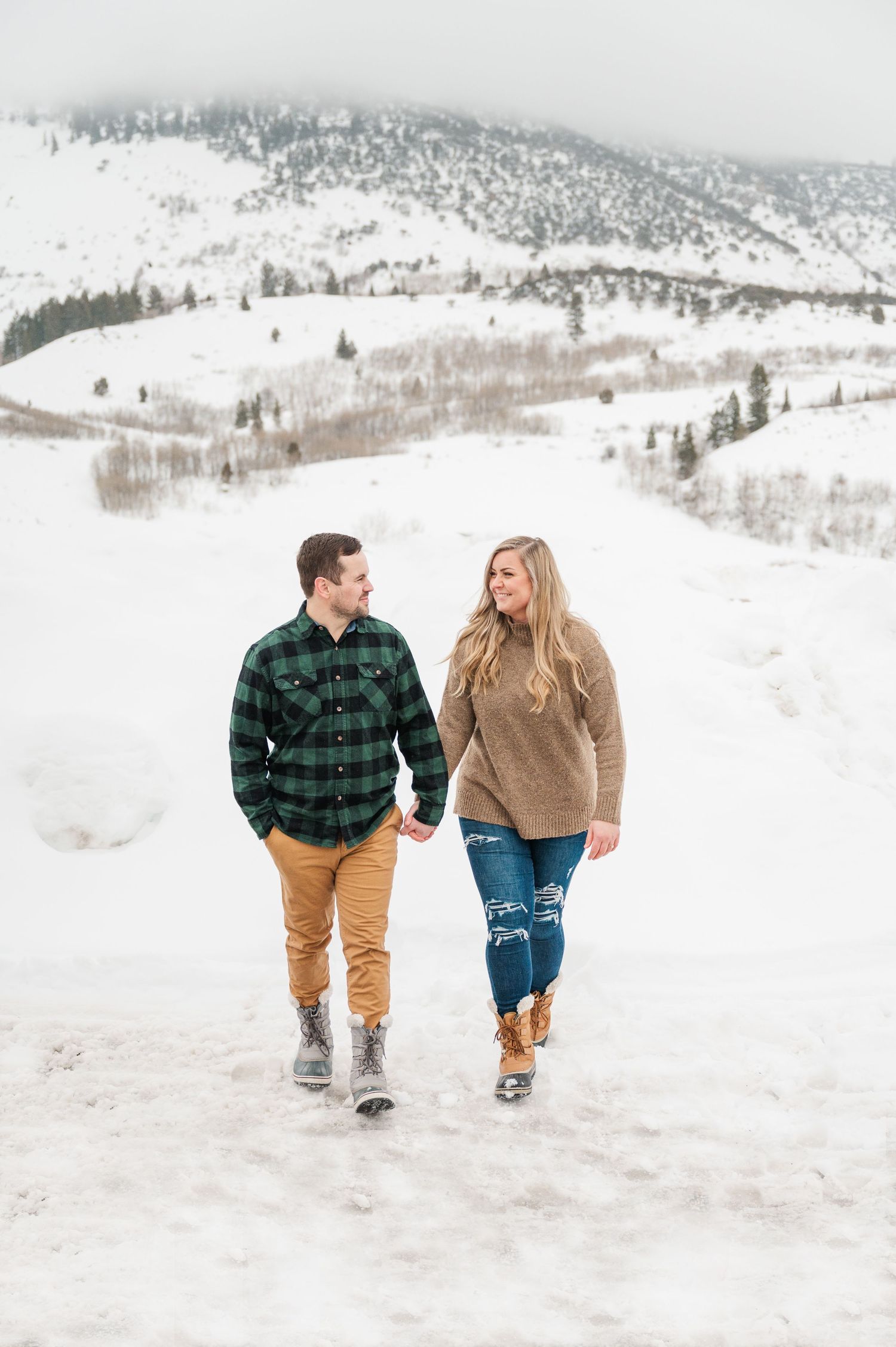 A couple walking hand in hand through a snowy mountain landscape.
