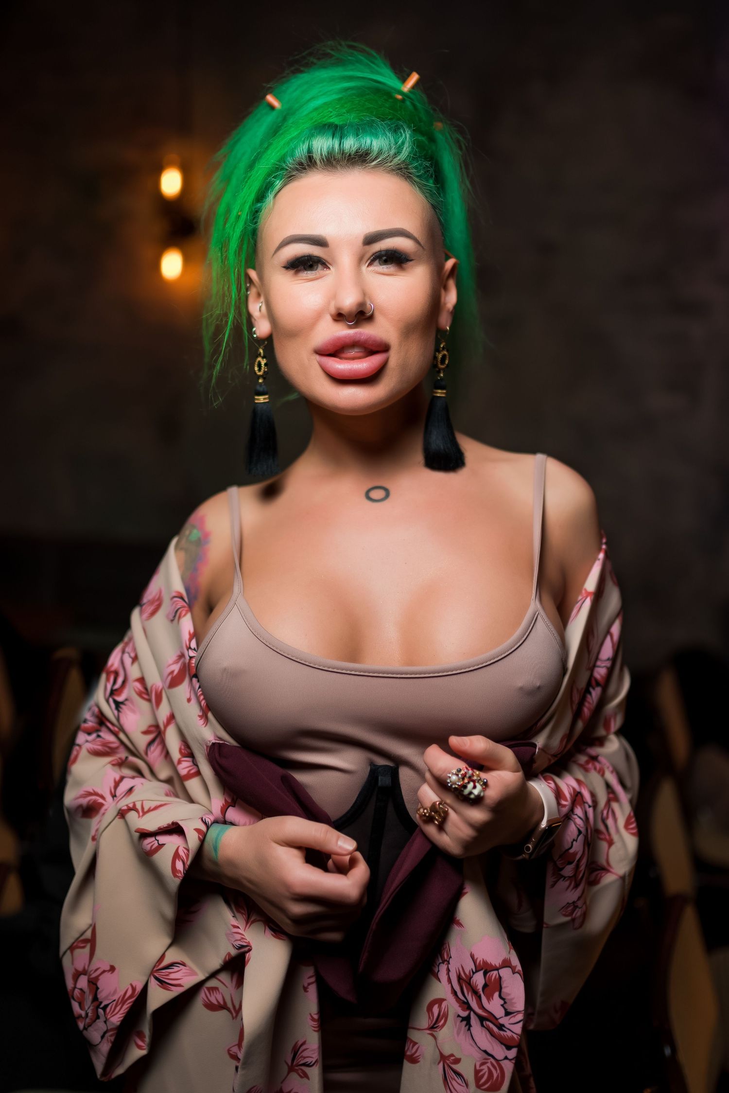 Bold portrait featuring vibrant green hair and floral print clothing in dim lighting.