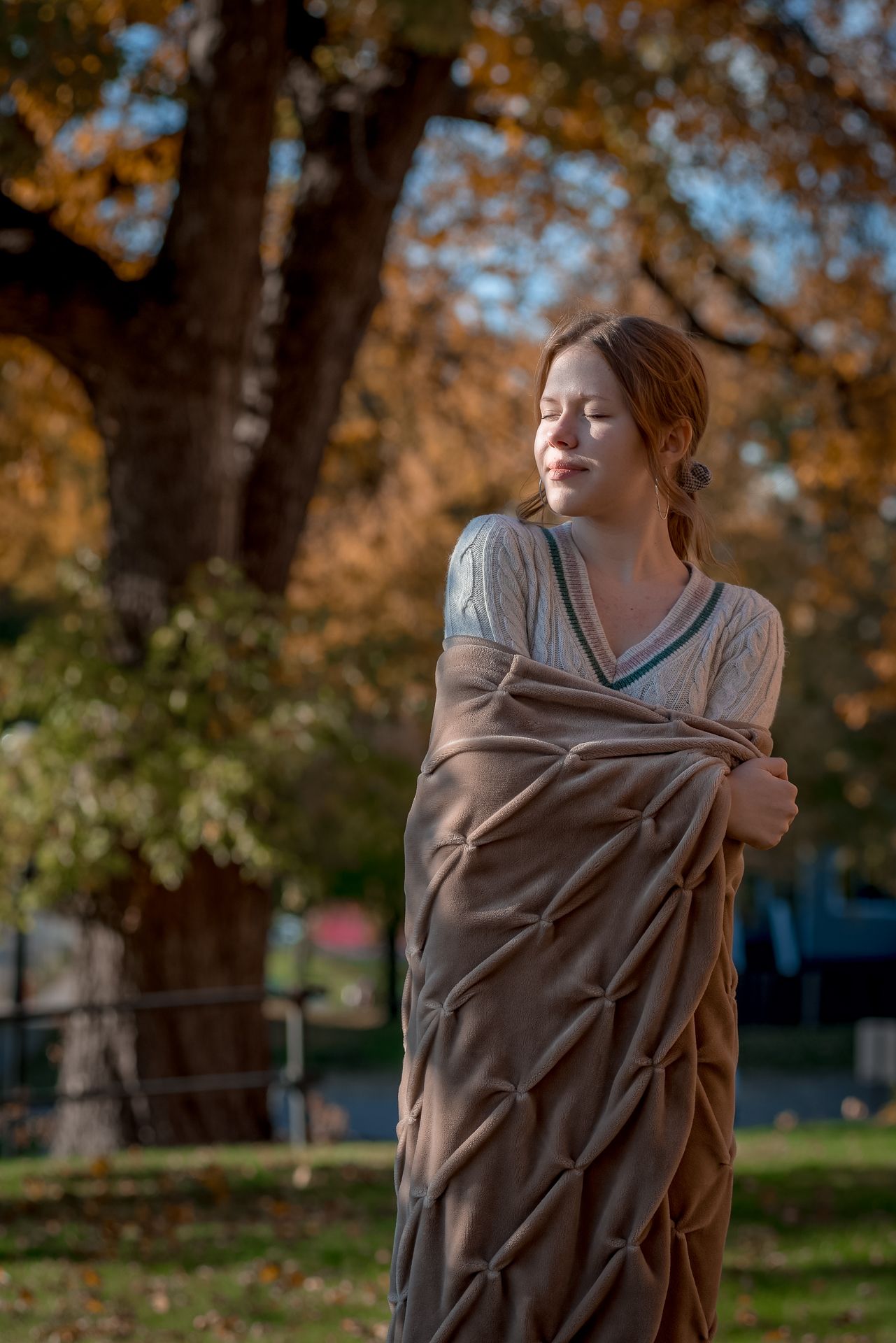 Autumn scene with fall foliage and wrapped in brown blanket.