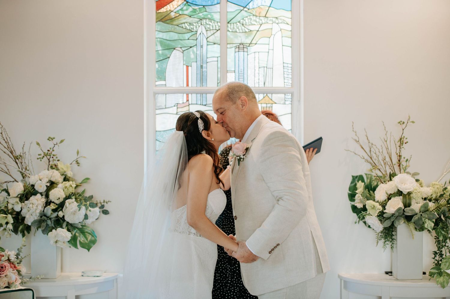 A romantic wedding ceremony moment in a chapel with stained glass windows and floral decorations.