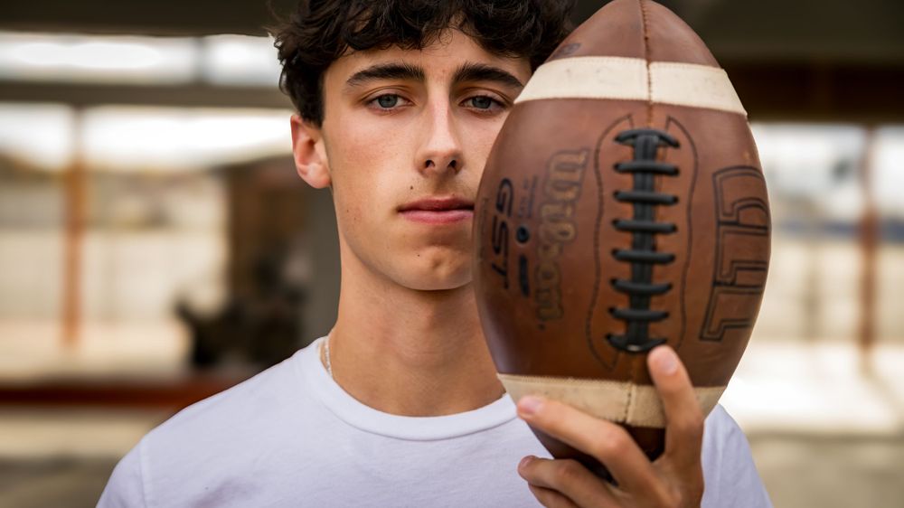 Teen athlete holds football while posing for portrait shot.