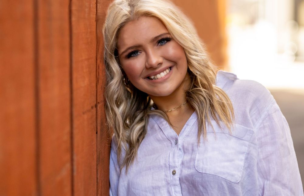 A casual portrait featuring someone in a white button-down shirt against an orange background.