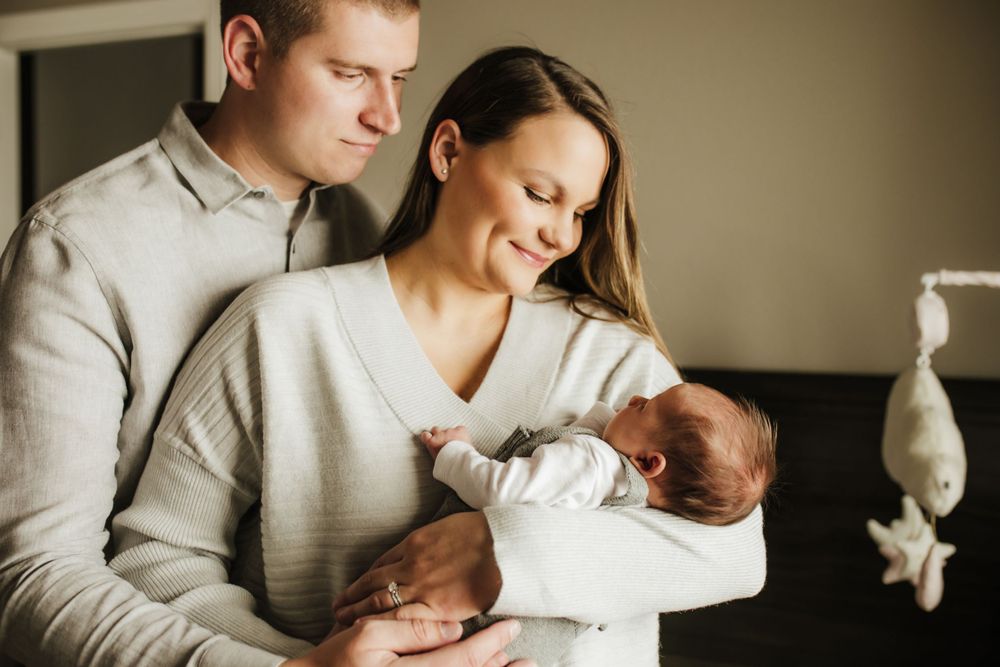 Parents tenderly cradle their newborn baby while standing together at home in soft lighting.