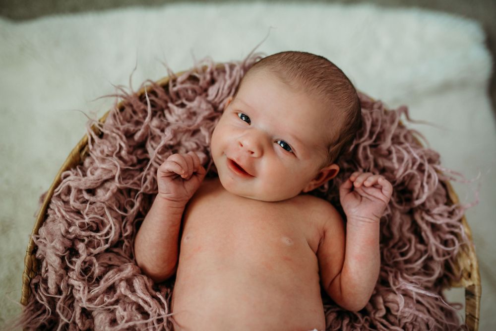 Adorable infant lies on soft pink textured blanket during professional newborn photography session.