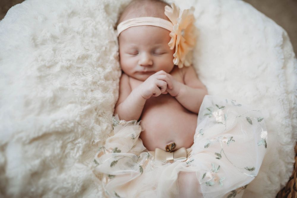 Newborn baby sleeping peacefully on white textured blanket wearing peach flower headband.