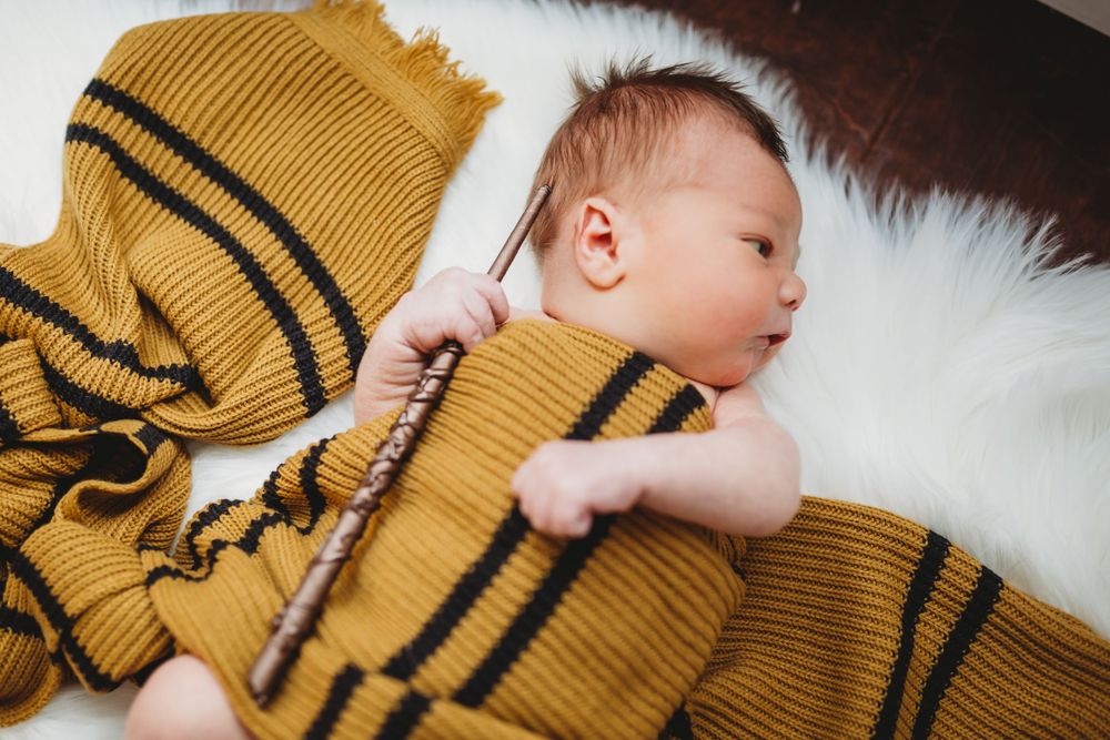 A sleeping baby rests on white fur wrapped in a mustard yellow knitted blanket with black stripes.
