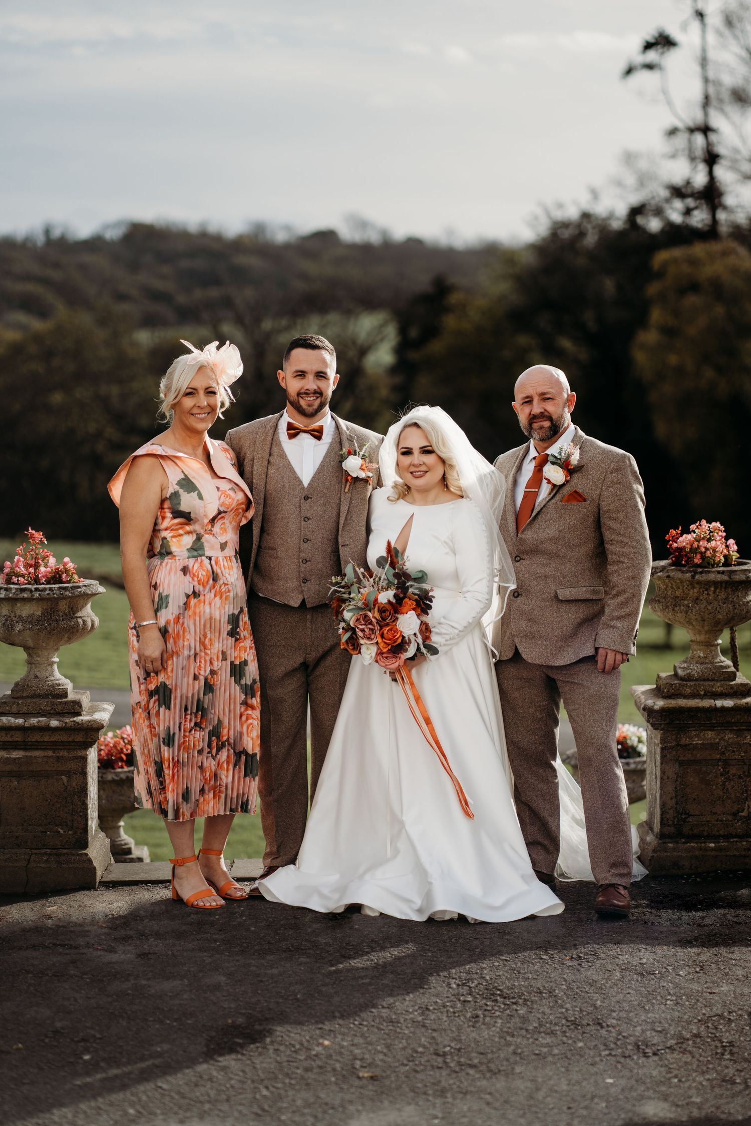 Wedding party poses outdoors in autumn with elegant floral arrangements and formal attire.