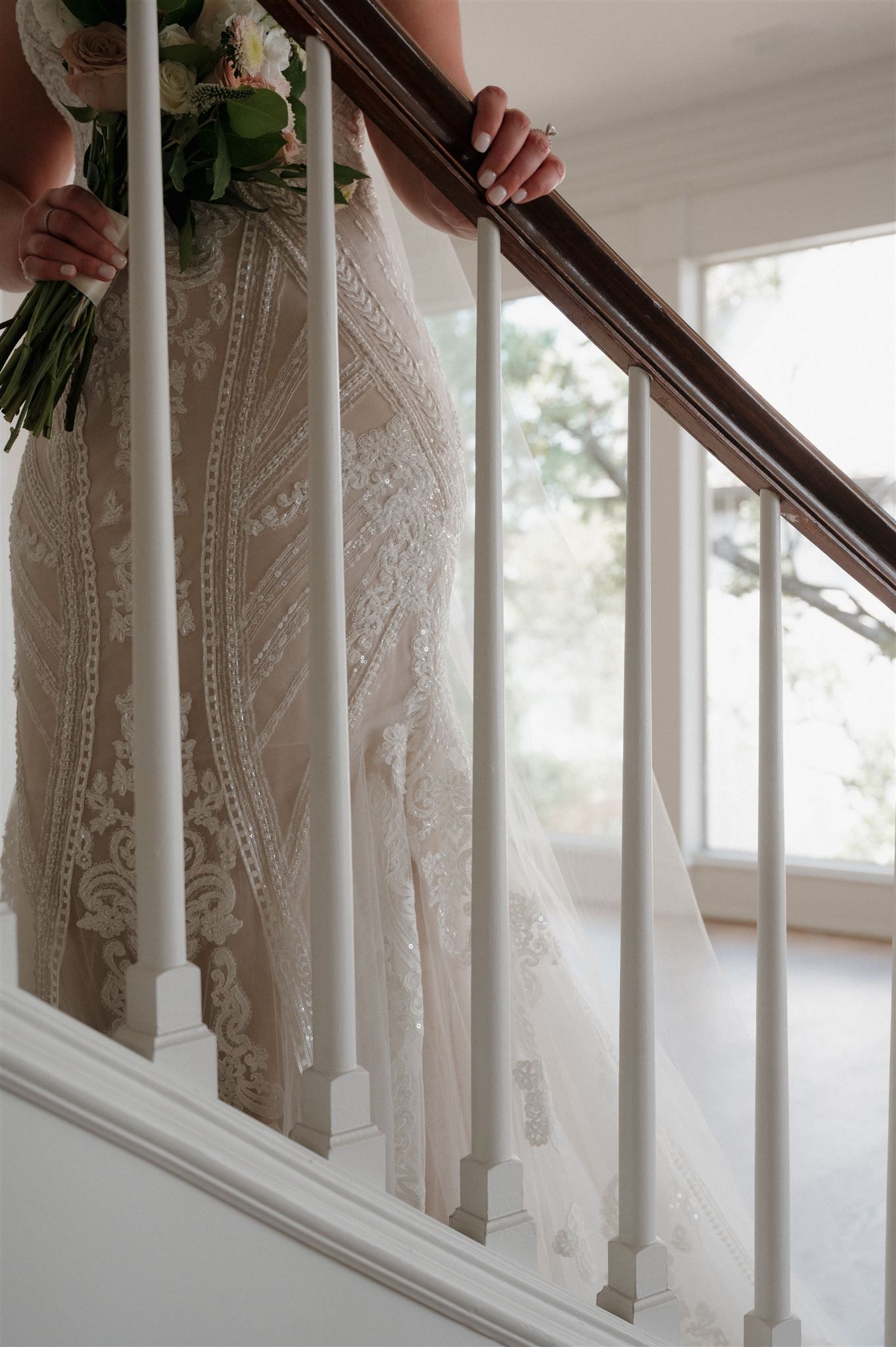 Detail shot of lace wedding dress and bouquet against white staircase balusters.