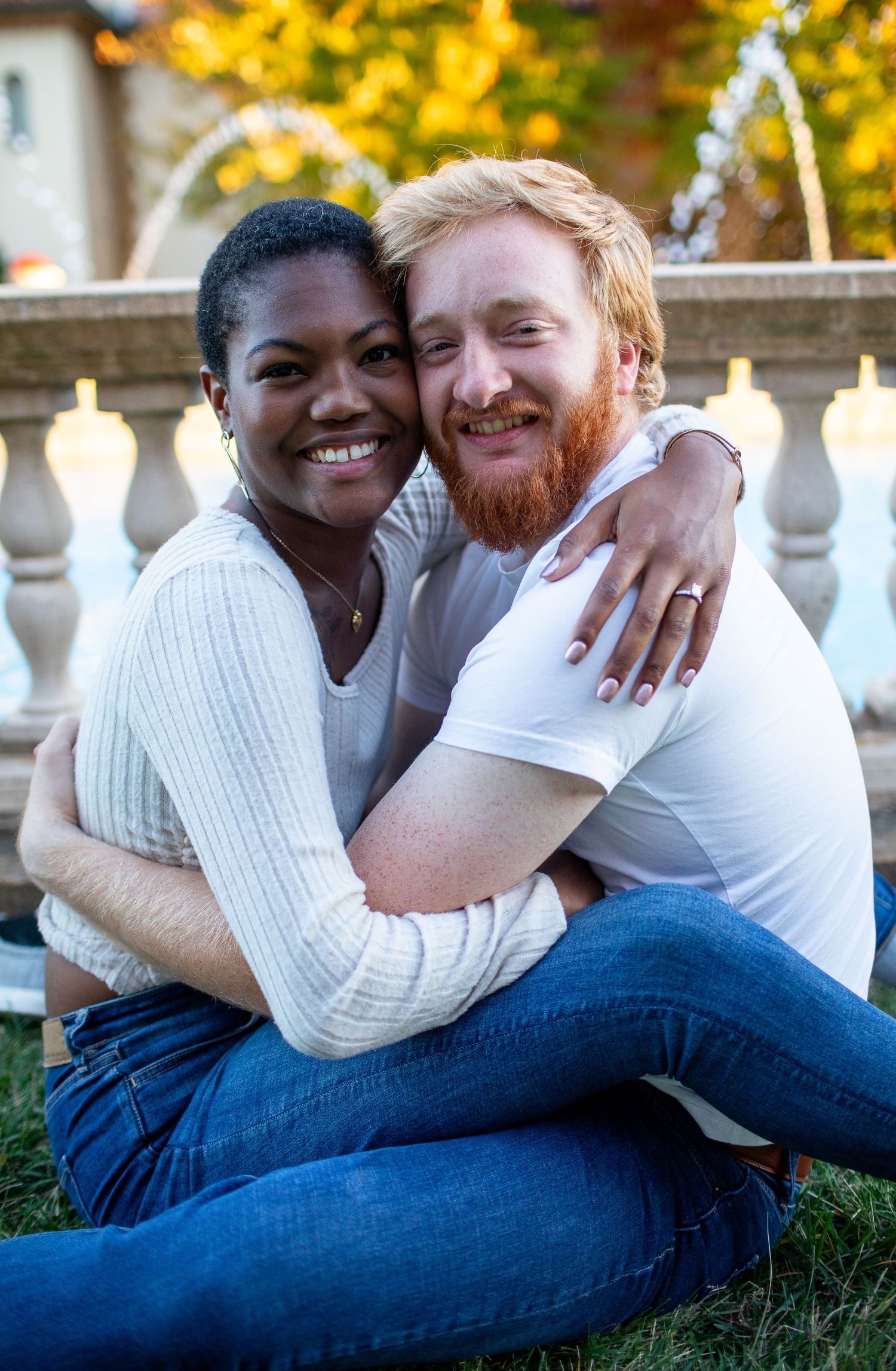 Happy couple embracing on lawn with fall foliage and classical architecture in background.