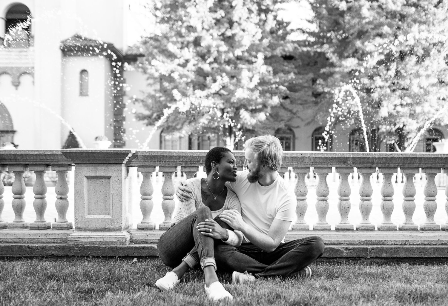 Couple relaxing on grass near ornate white balustrade in black and white portrait.
