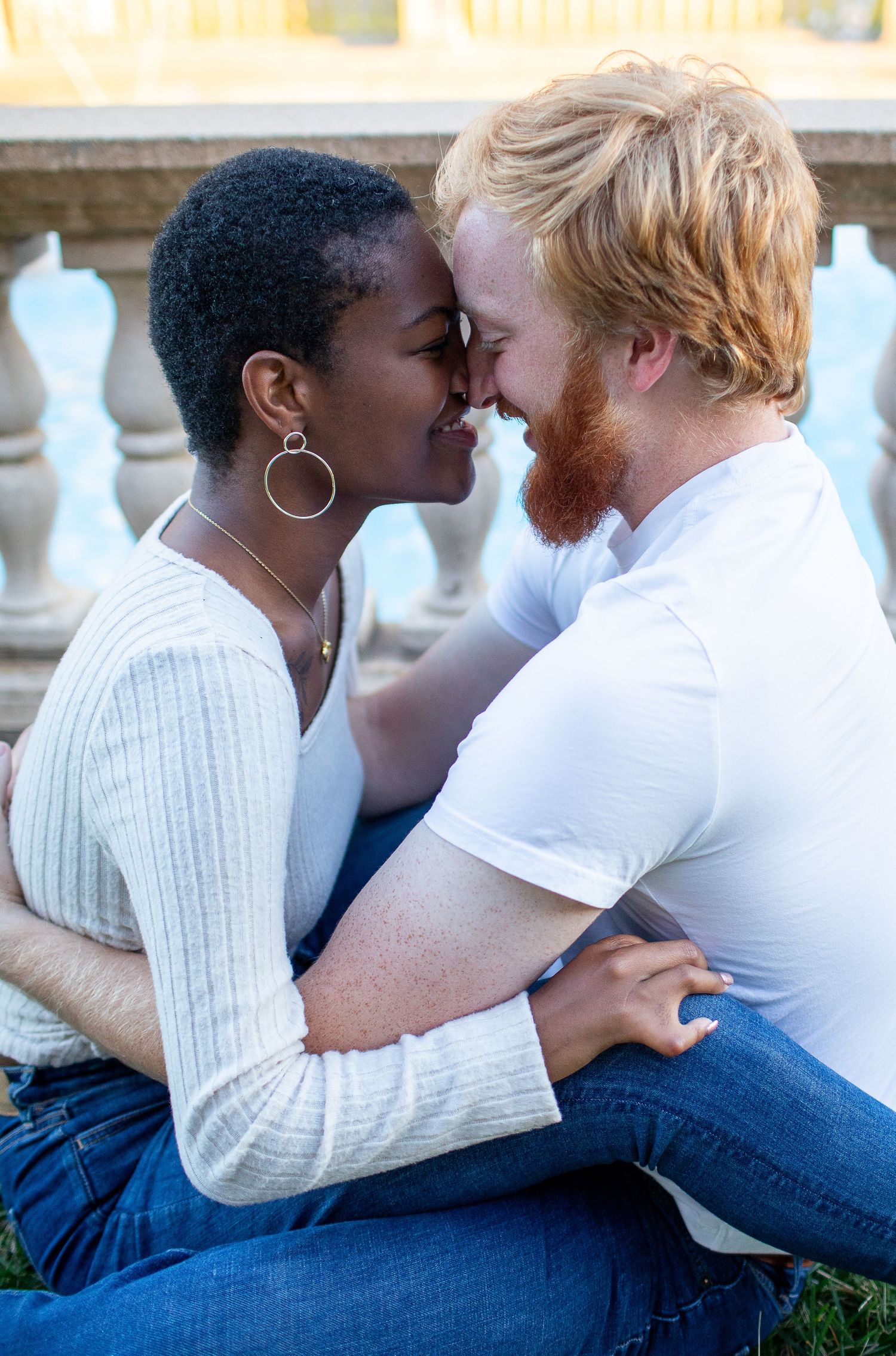 Tender intimate moment between couple sitting on grass near decorative railing.