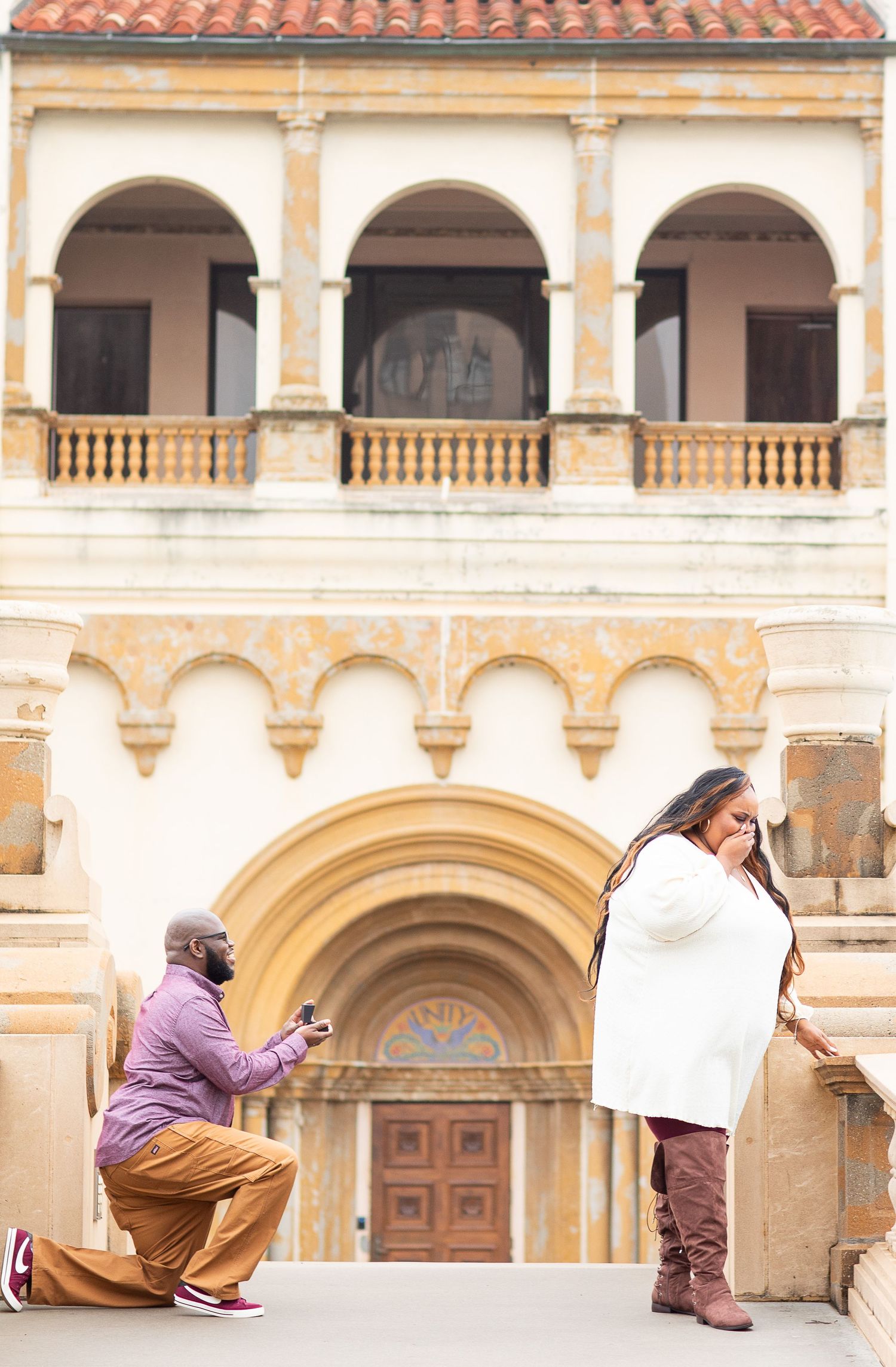 A proposal moment captured at a historic building with Spanish colonial architecture and arched windows.
