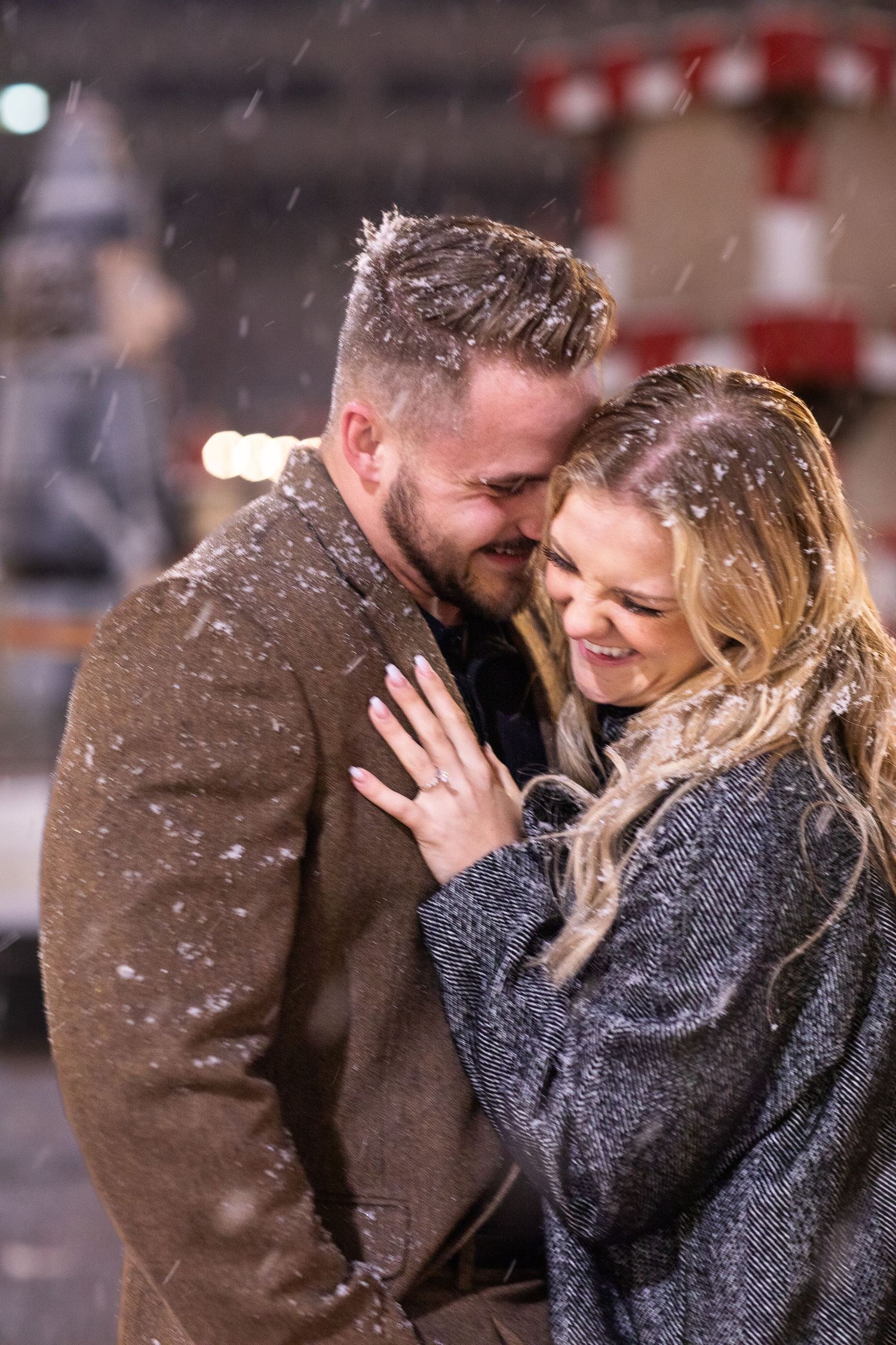 Couple embraces and laughs together as snow falls around them at night.