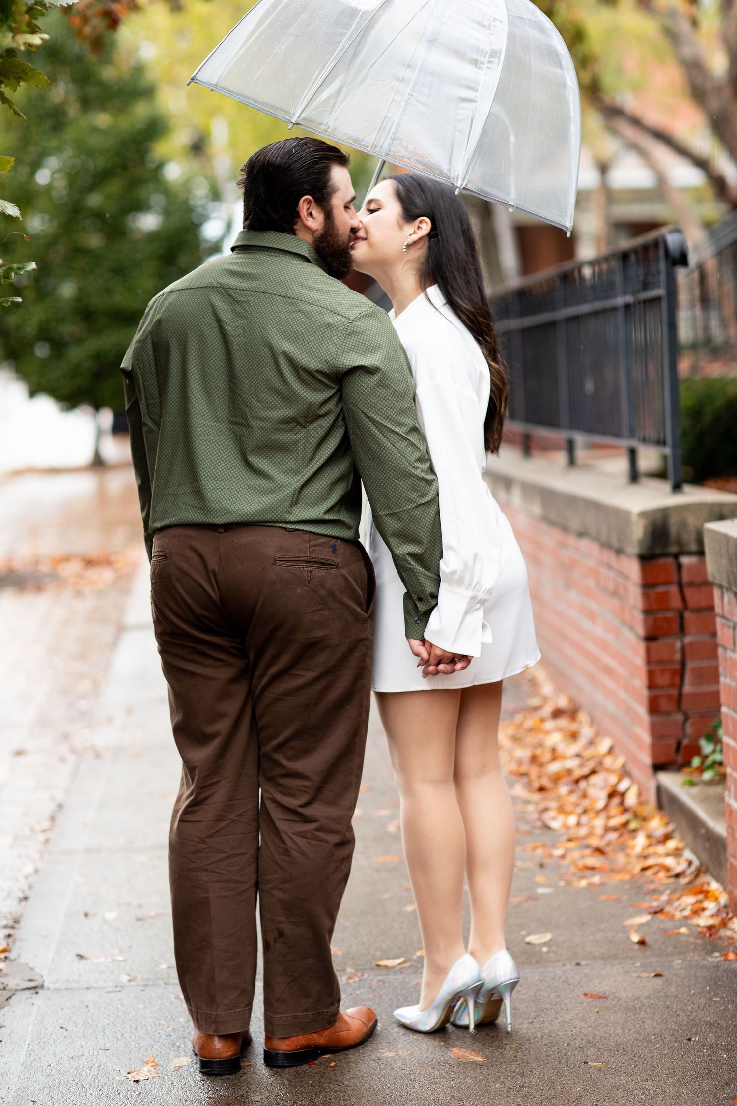 Couple sharing intimate moment under clear umbrella on leaf-covered street.