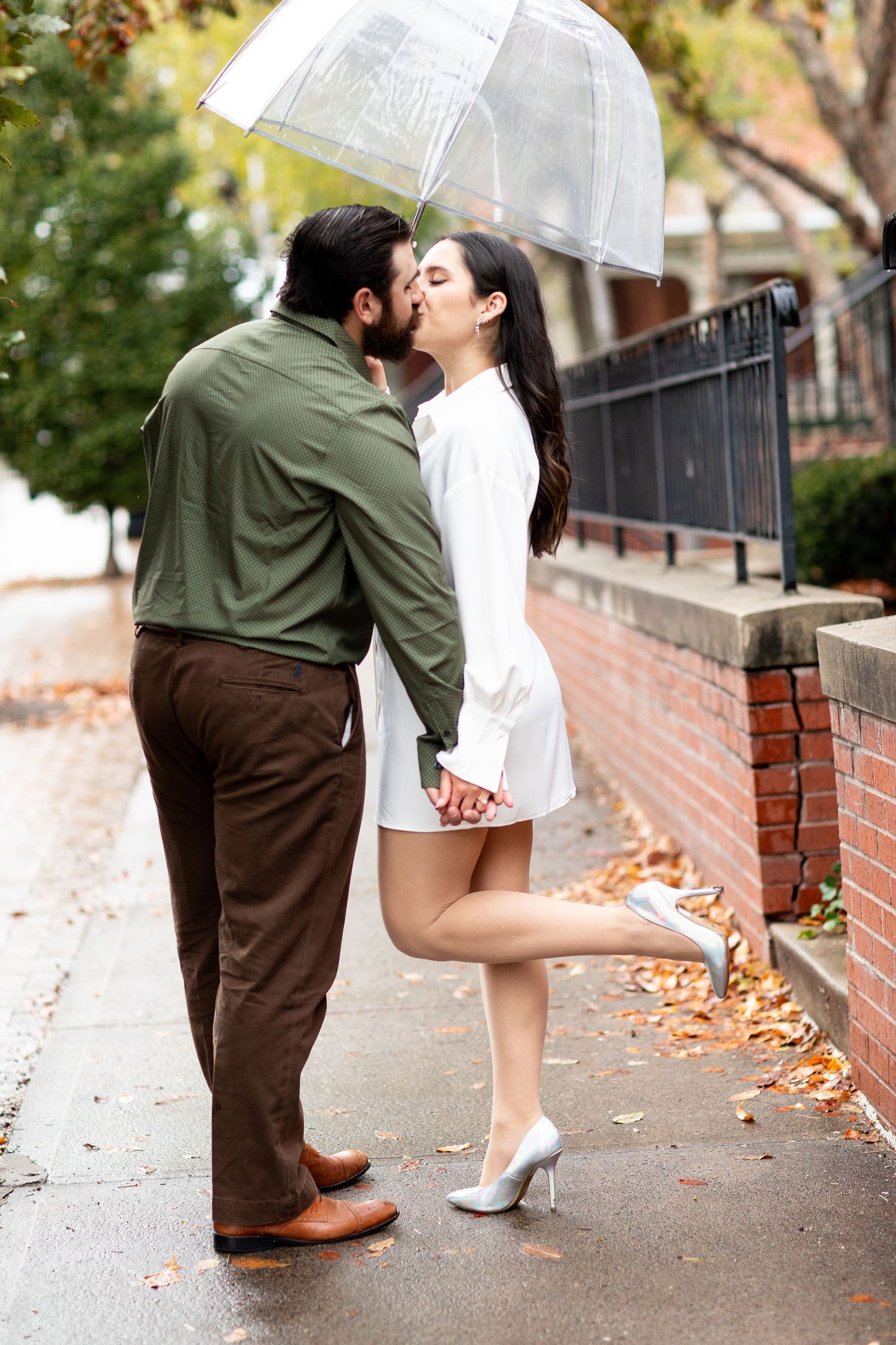 Romantic moment under clear umbrella on rainy autumn sidewalk.