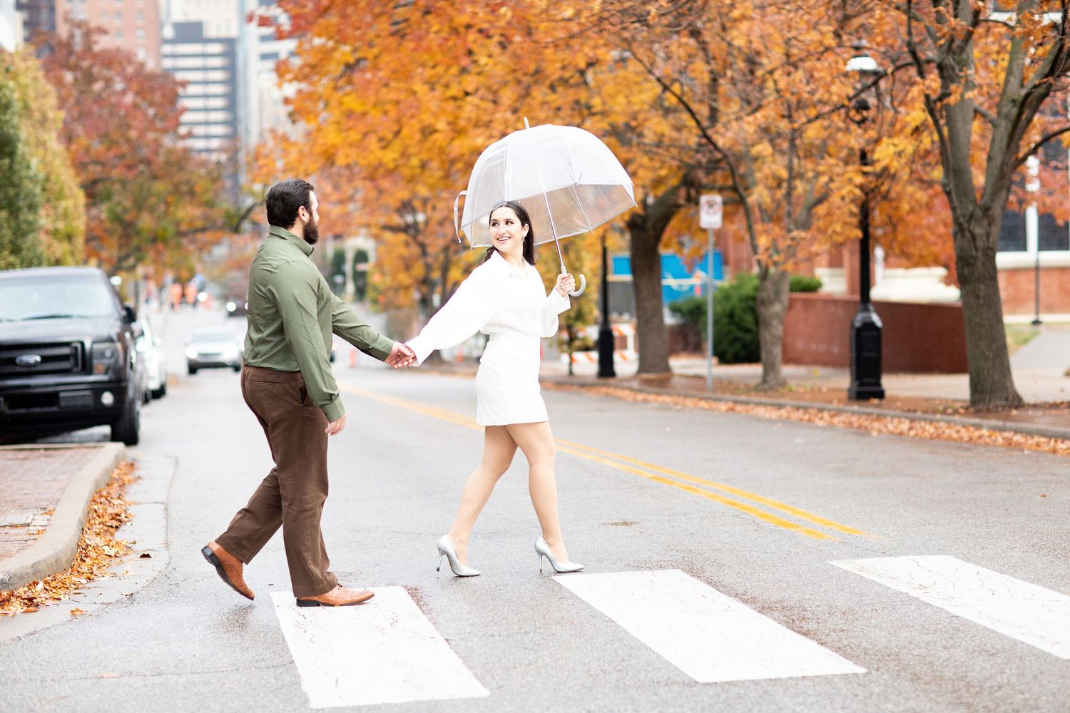 Couple with clear umbrella posing playfully on autumn crosswalk.