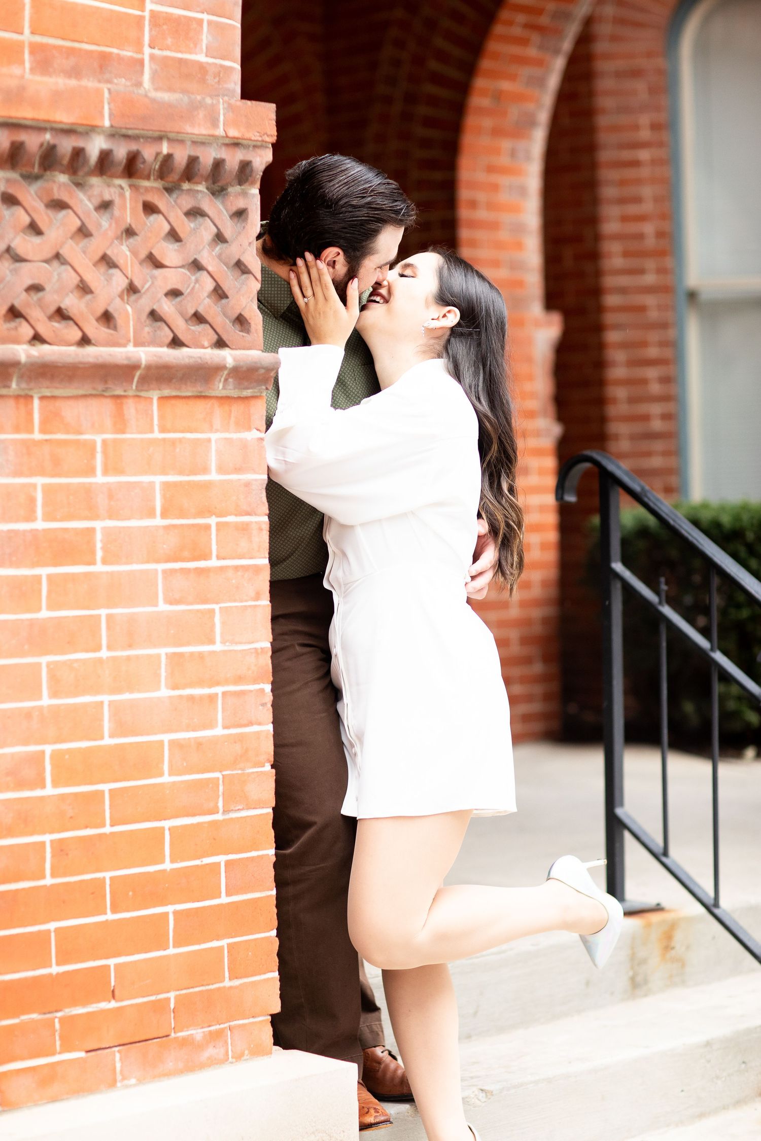 Romantic embrace against brick building with decorative lattice detail.