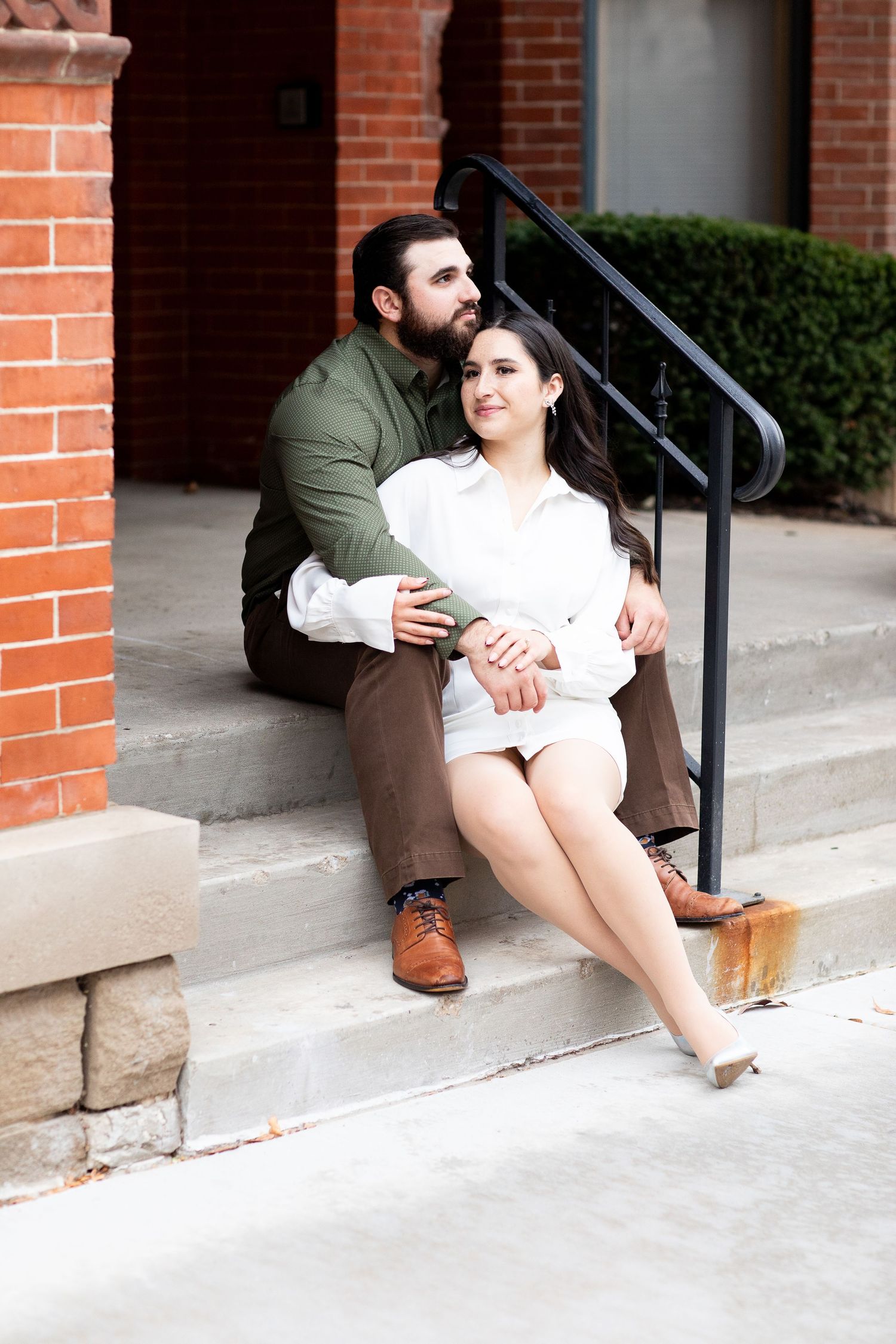 Couple sitting together on concrete steps near a brick wall and black railing.