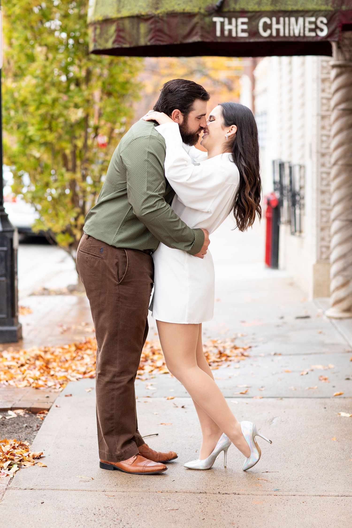 Couple sharing an intimate moment under The Chimes sign with fall foliage in the background.