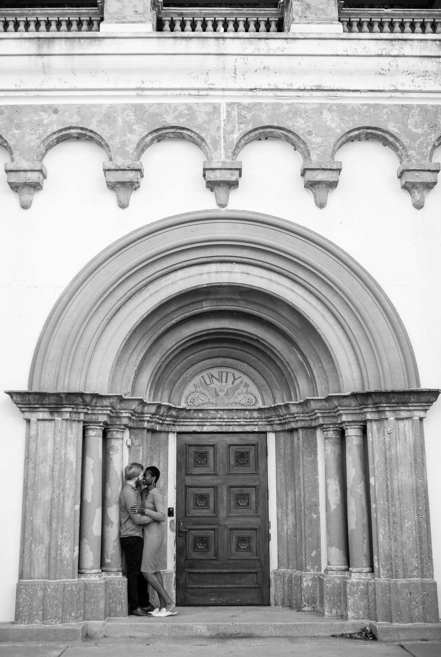 Black and white portrait of couple standing in arched doorway of historic building.