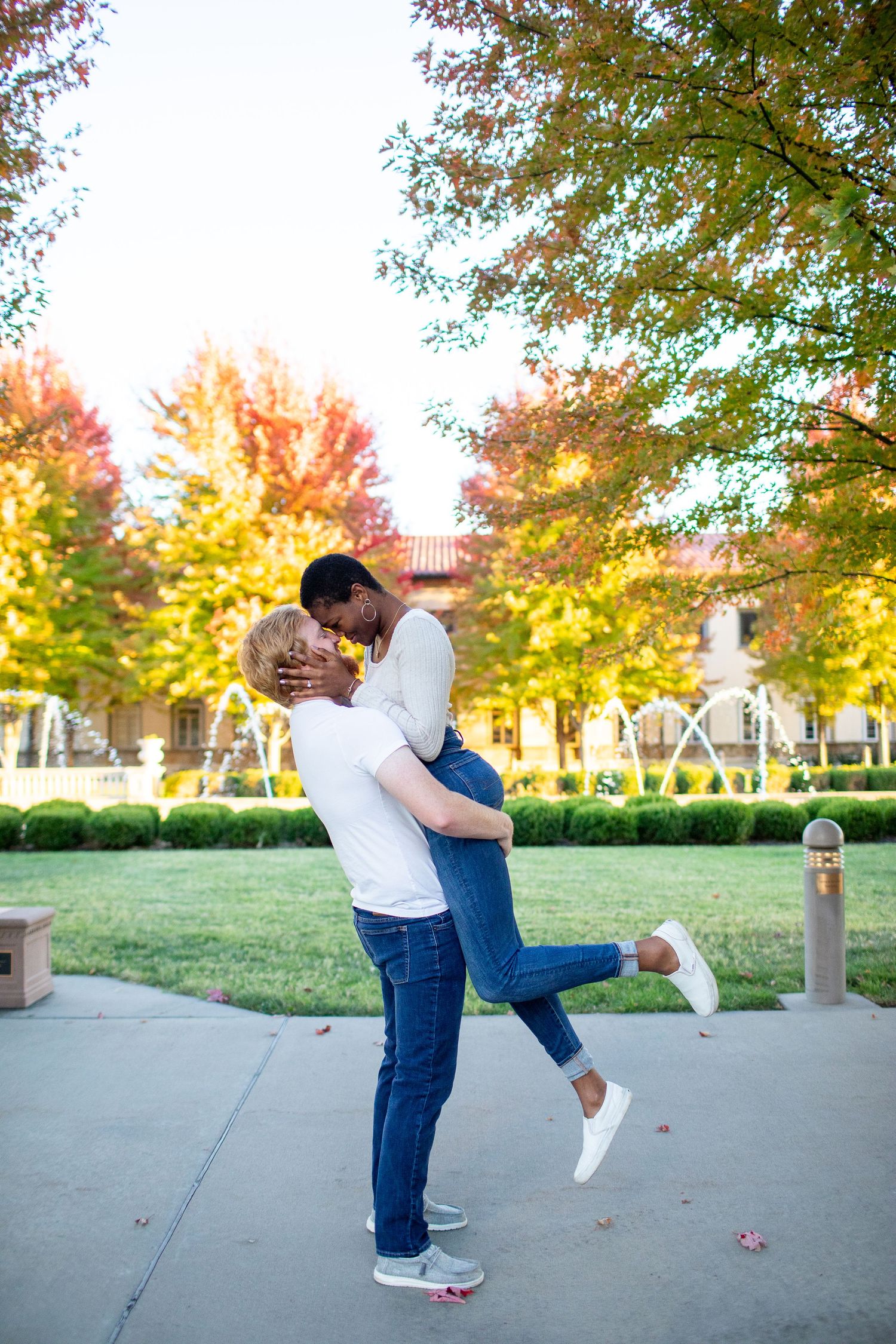 Playful romantic moment with couple in autumn courtyard with colorful fall foliage.