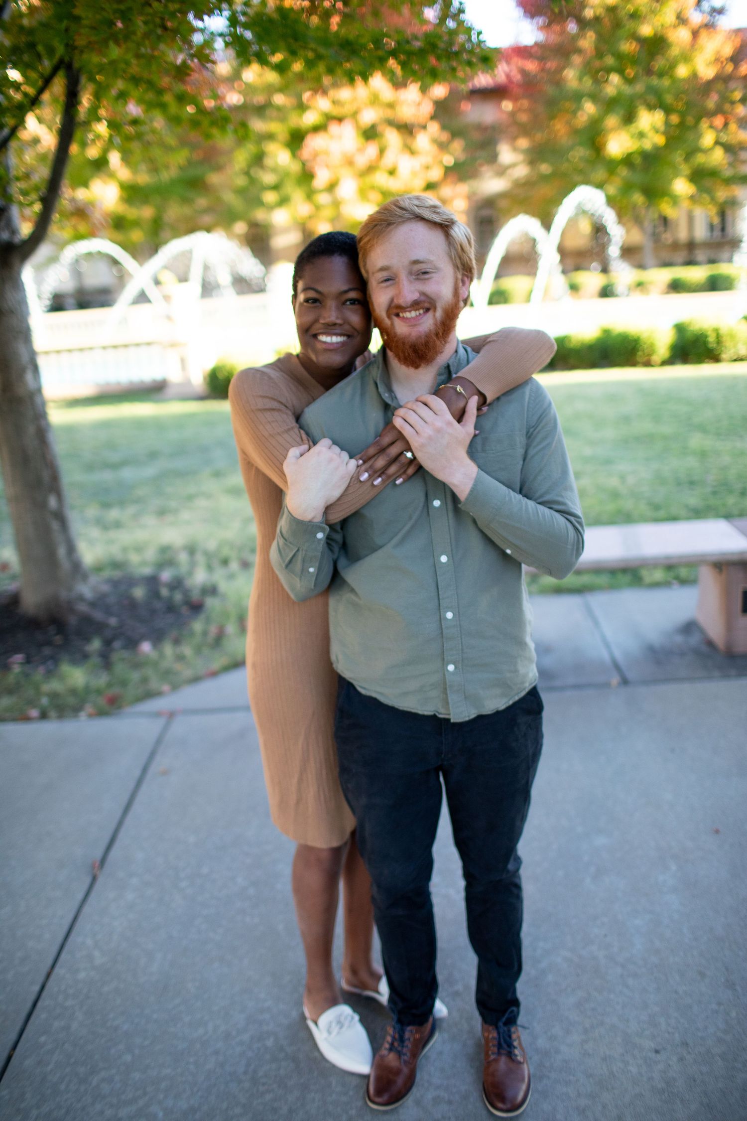 Joyful couple sharing a warm embrace while standing on a pathway with fall foliage in the background.
