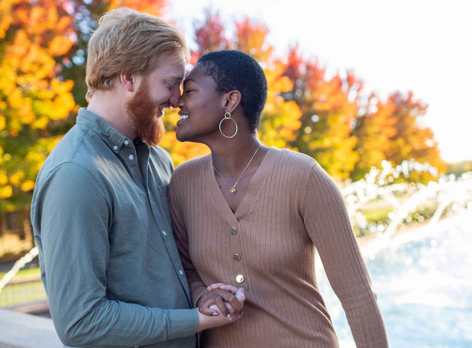 Romantic couple in casual attire sharing a tender moment against vibrant fall colors.