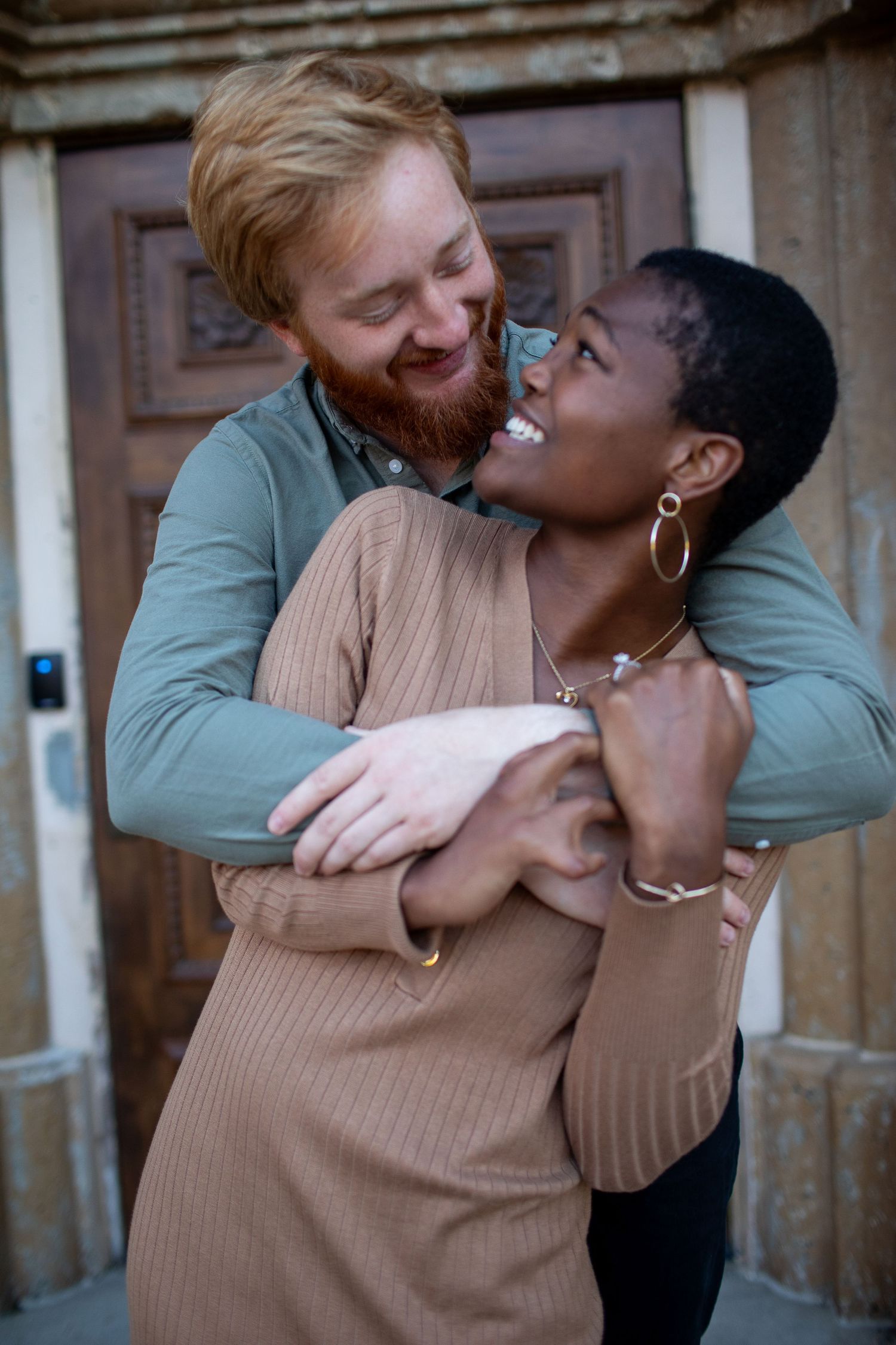 Intimate couple sharing joyful laughter and embrace in front of vintage wooden door.